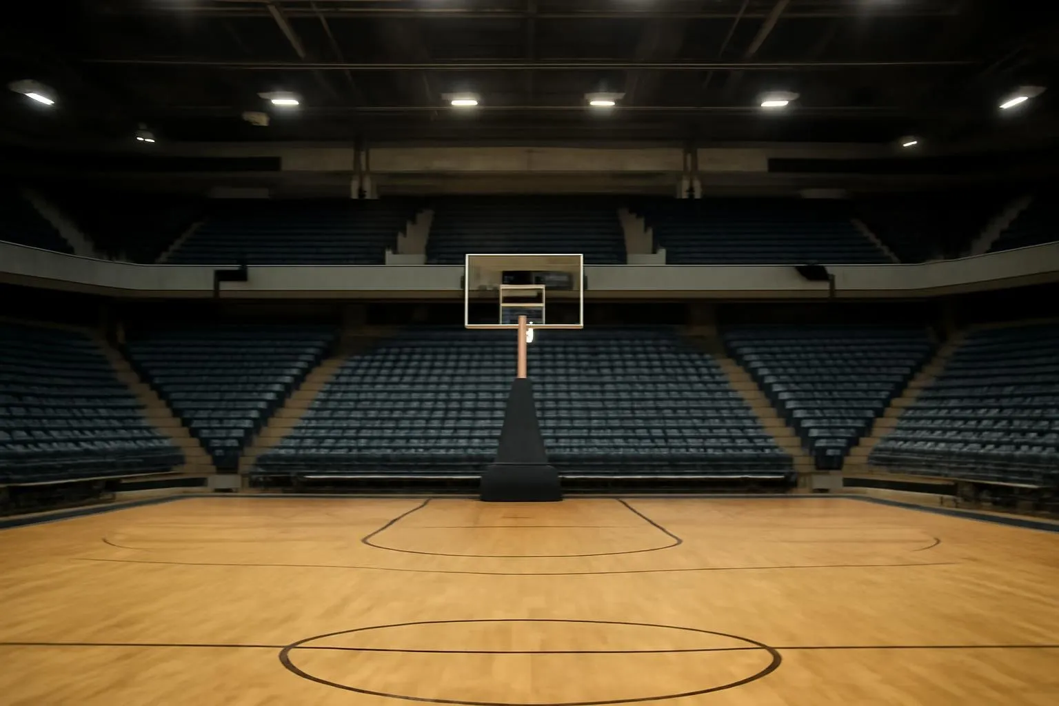 Wide-angle interior view of an empty indoor basketball arena, hardwood court lit by arena lights.