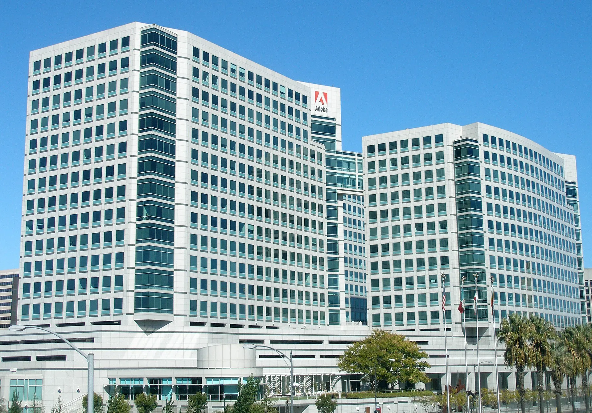 Adobe's headquarters office towers in San Jose, California, with the company's red logo, under a clear blue sky.