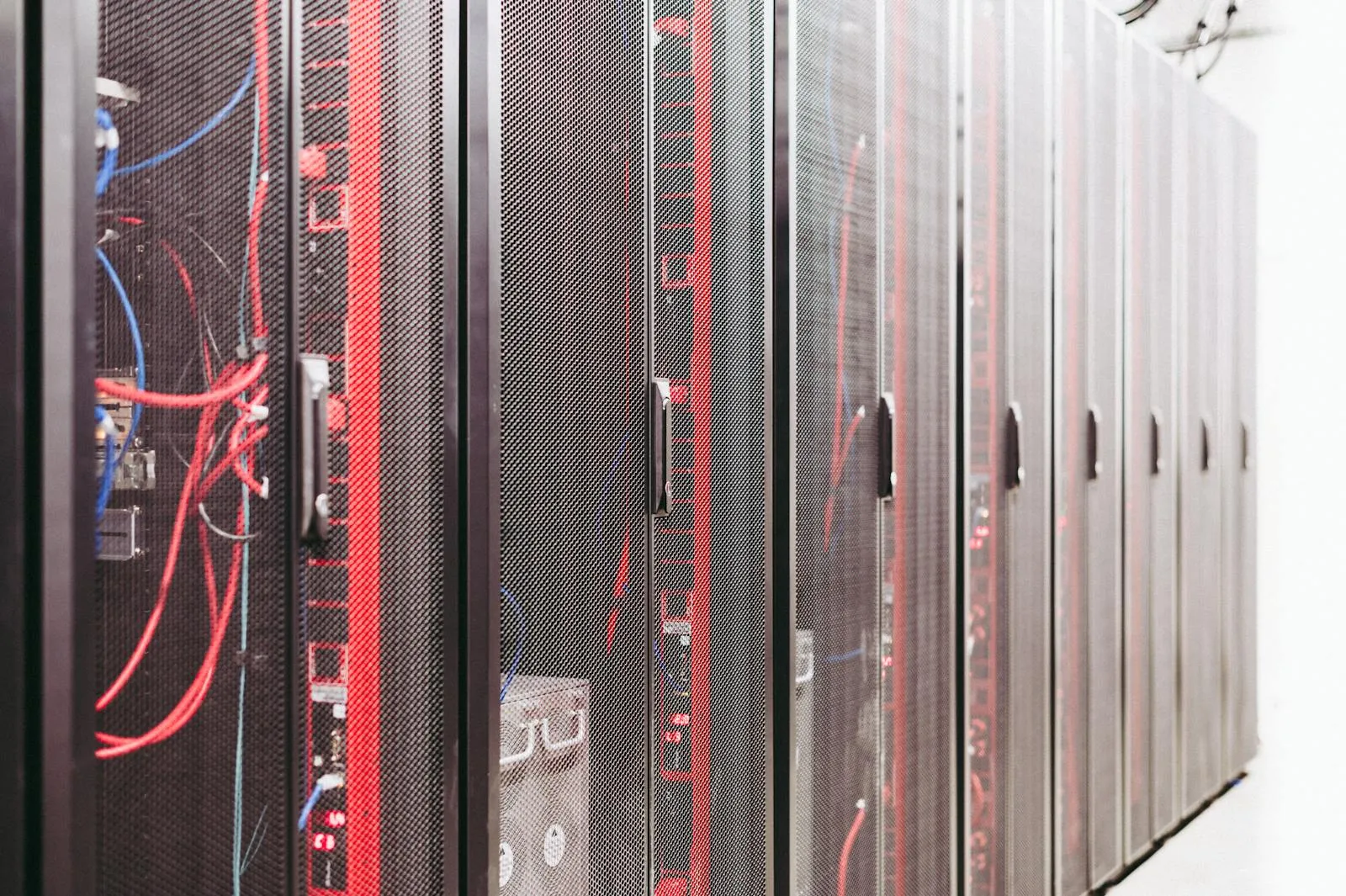 A row of dark server racks threaded with red and blue cabling inside a data center.