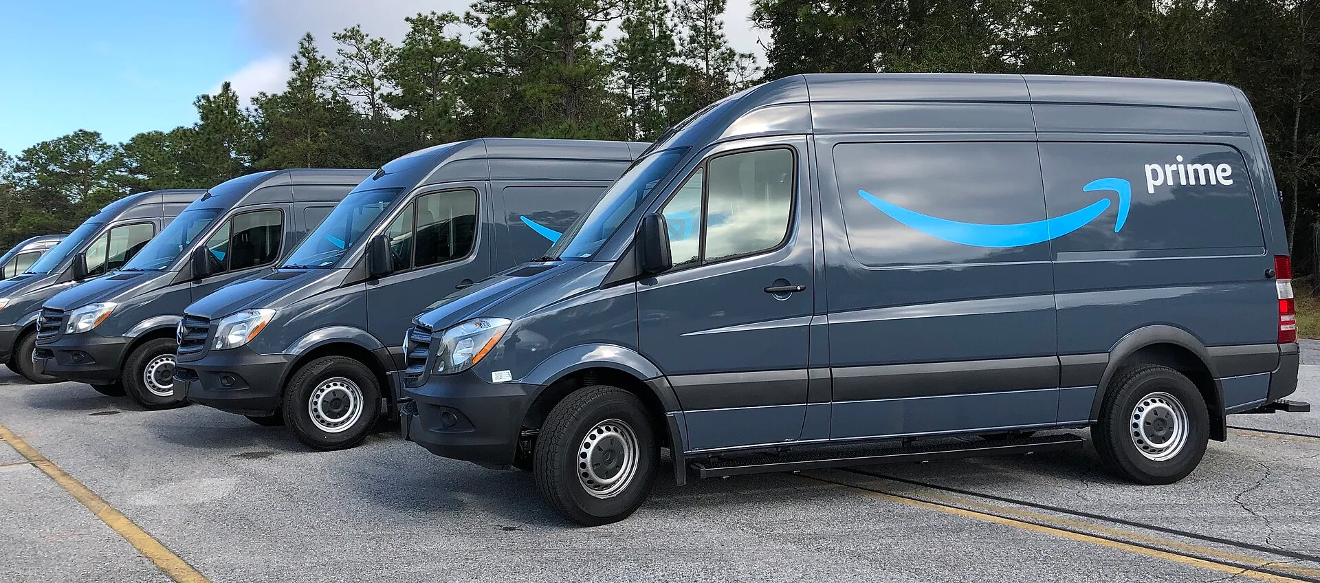 A row of dark gray Amazon Prime delivery vans parked side by side, each marked with the blue Prime smile logo.