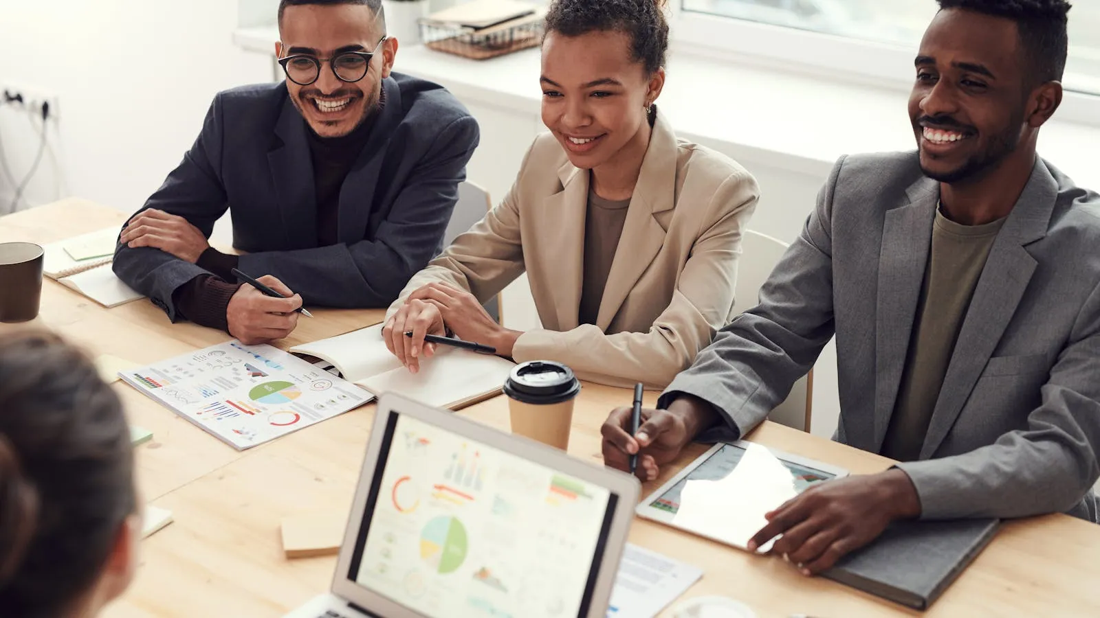 Three professionals in business attire reviewing charts and graphs at a workplace meeting table.