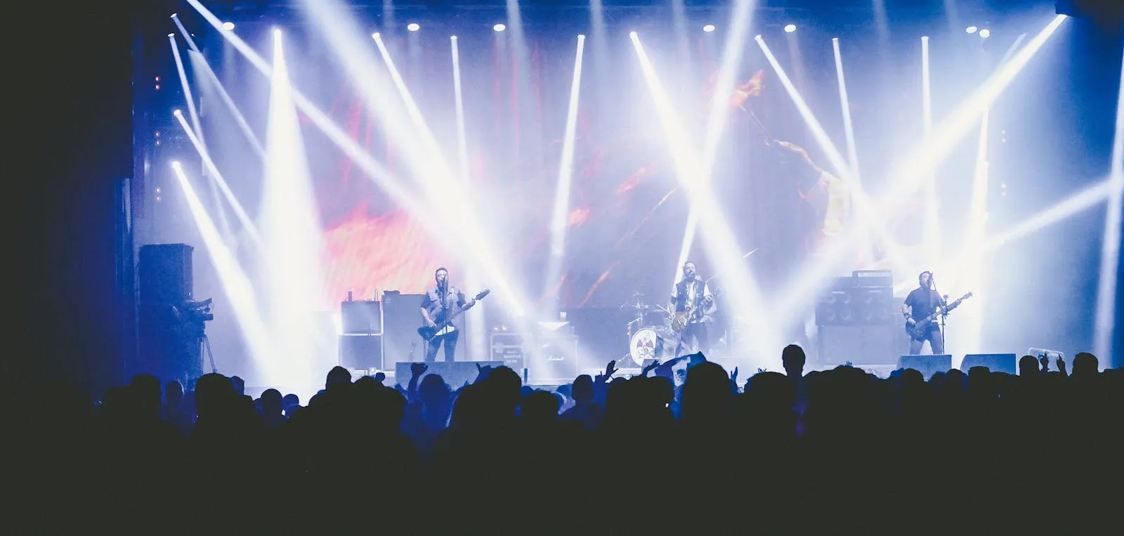 Wide-angle view of a packed concert arena with a performer on stage under colorful lights, crowd stretching into the distance
