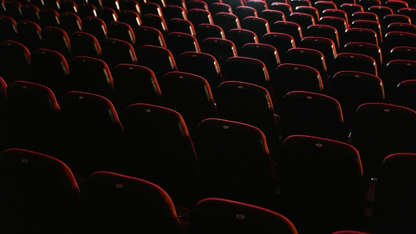 Rows of empty red seats fade into darkness inside a dimly lit movie theater
