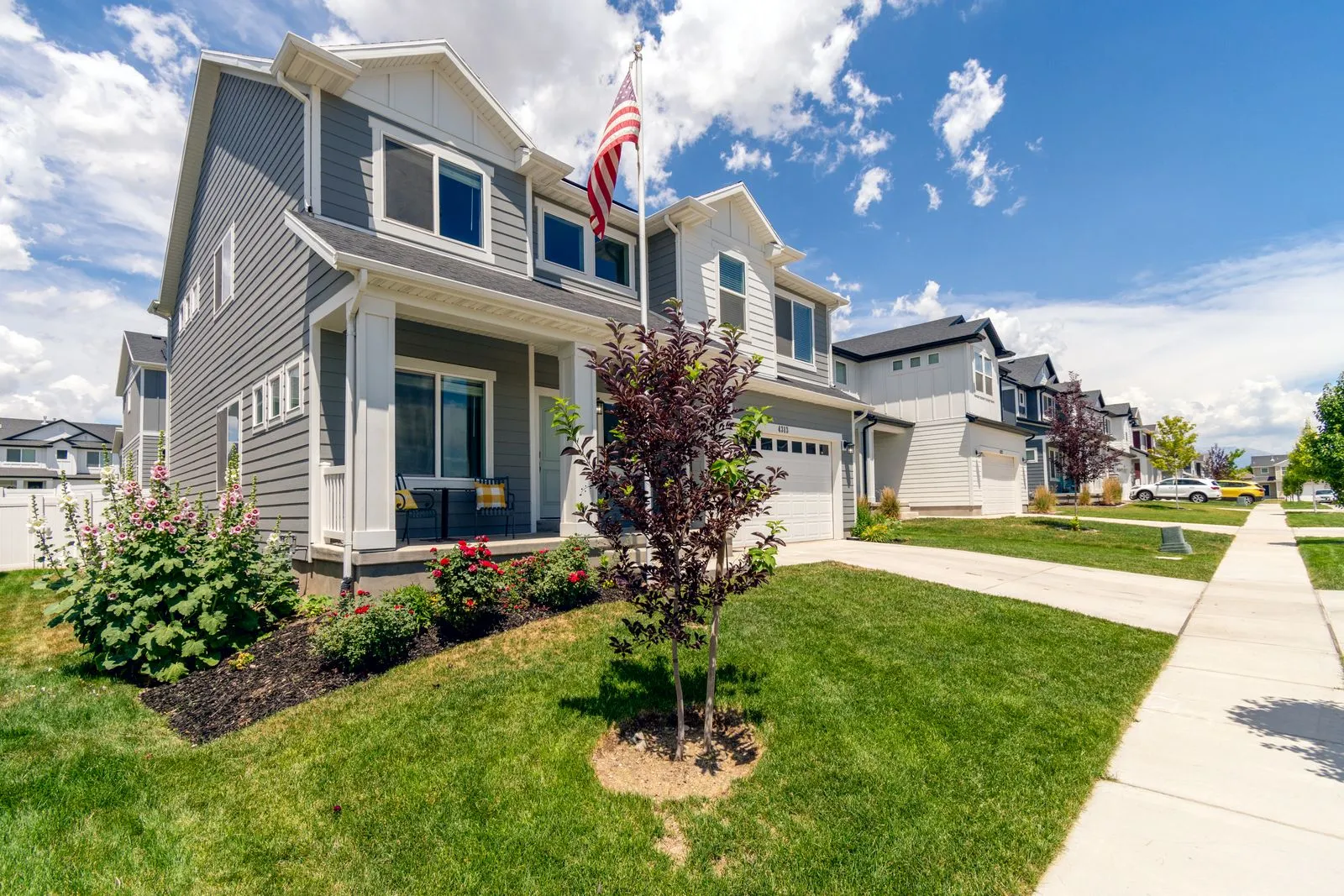 Newly built single-family homes with fresh landscaping along a sunny suburban street, an American flag out front