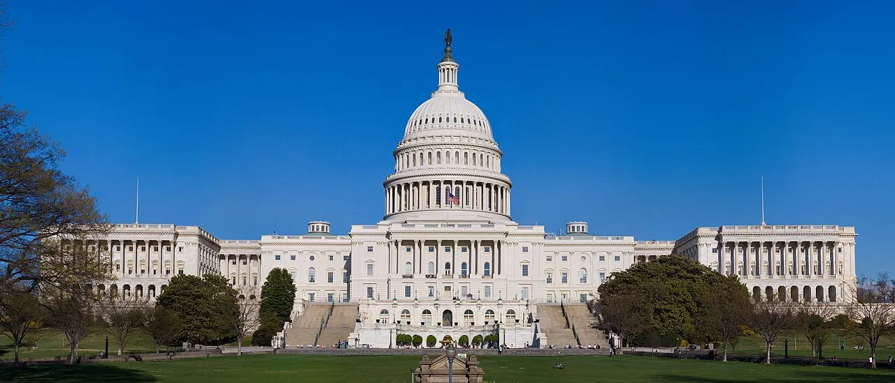 The western front of the United States Capitol building showing the central dome and both legislative wings against a blue sky
