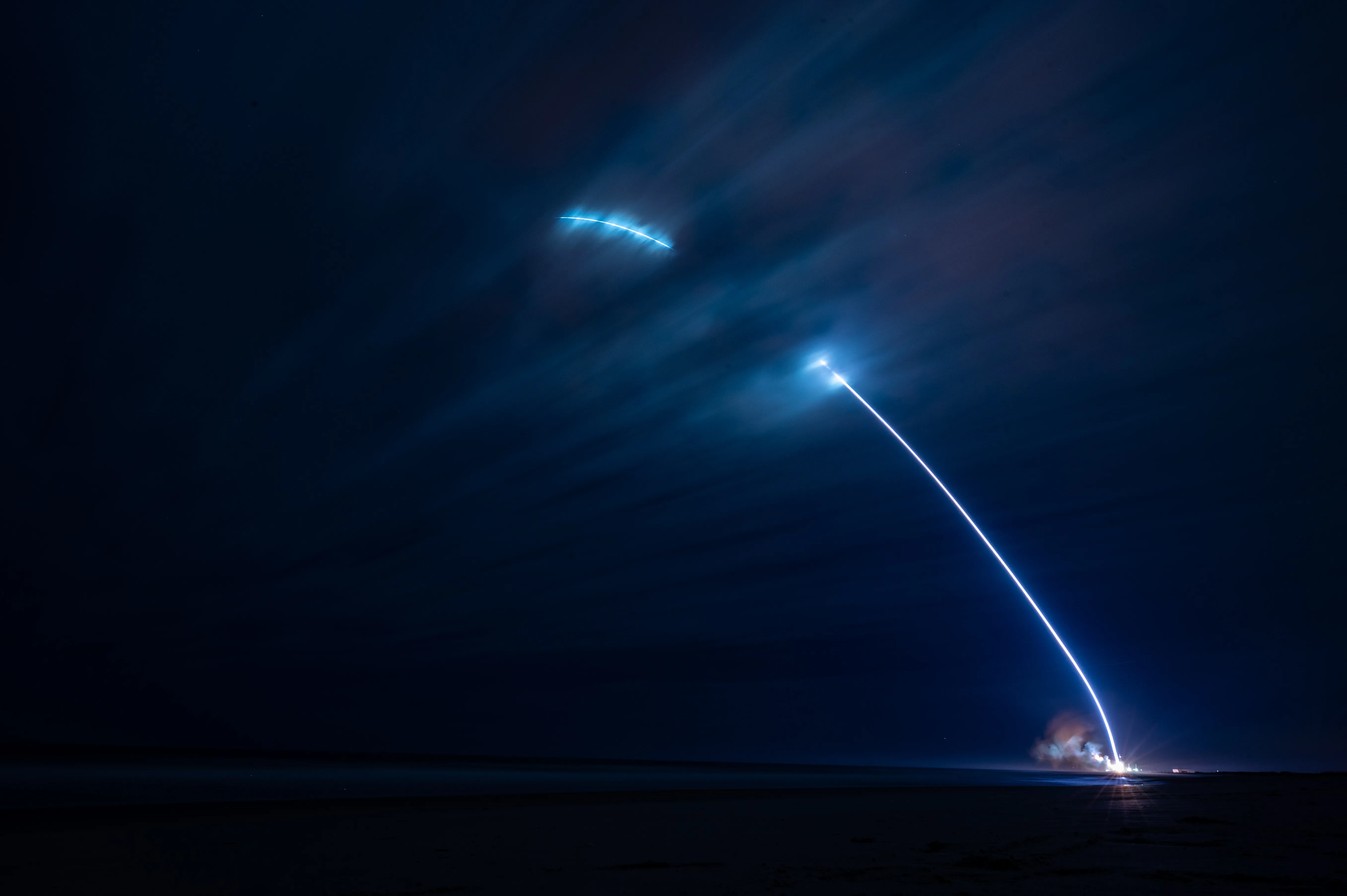 Long-exposure photograph of Blue Origin's New Glenn rocket ascending from Launch Complex 36 at Cape Canaveral Space Force Station at night, leaving a bright arc of flame against the dark sky