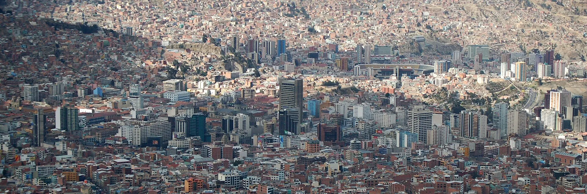 A panoramic view of La Paz, Bolivia, with dense low-rise buildings filling a valley and climbing the surrounding hillsides.