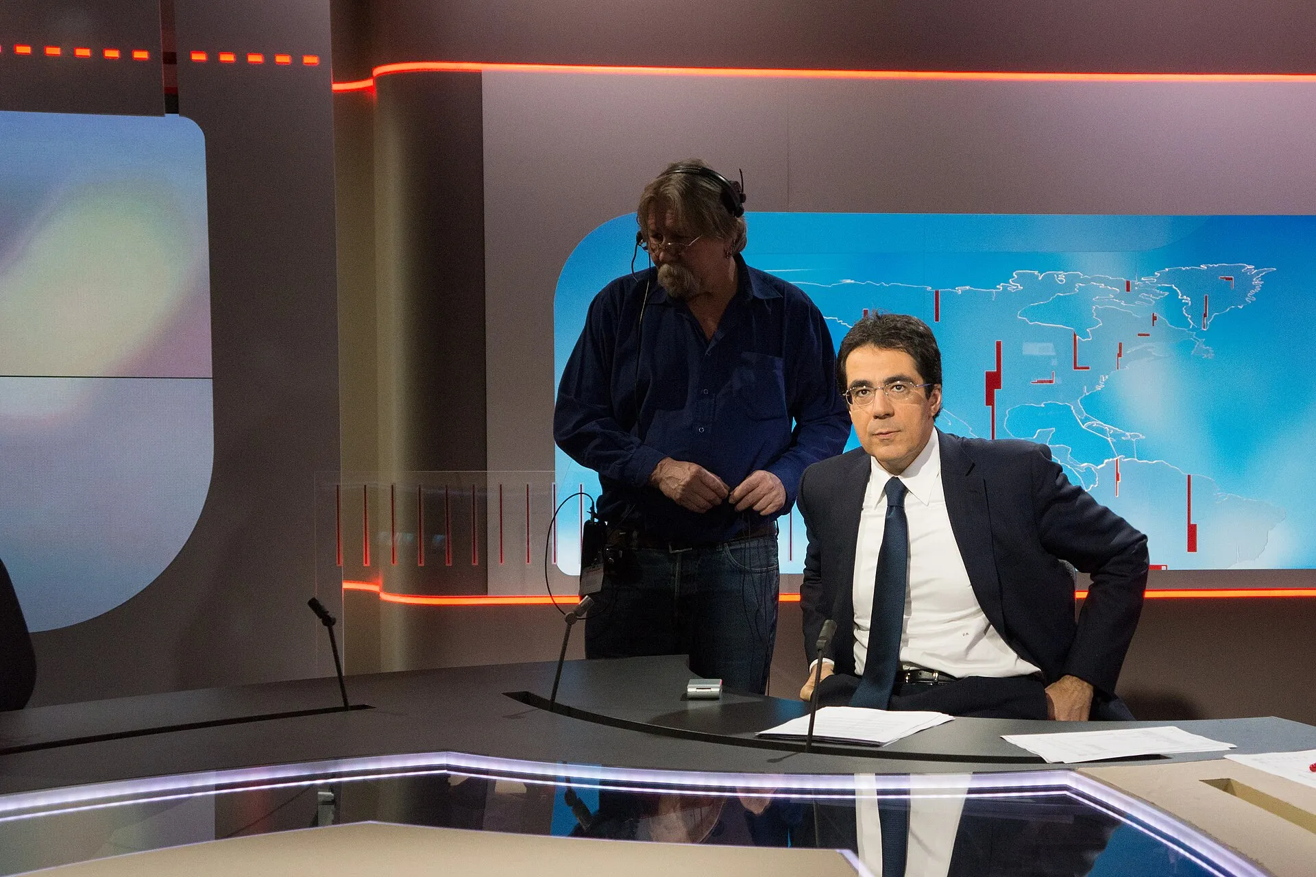 Interior of a television news studio with an anchor desk, monitors and overhead lighting rigs.