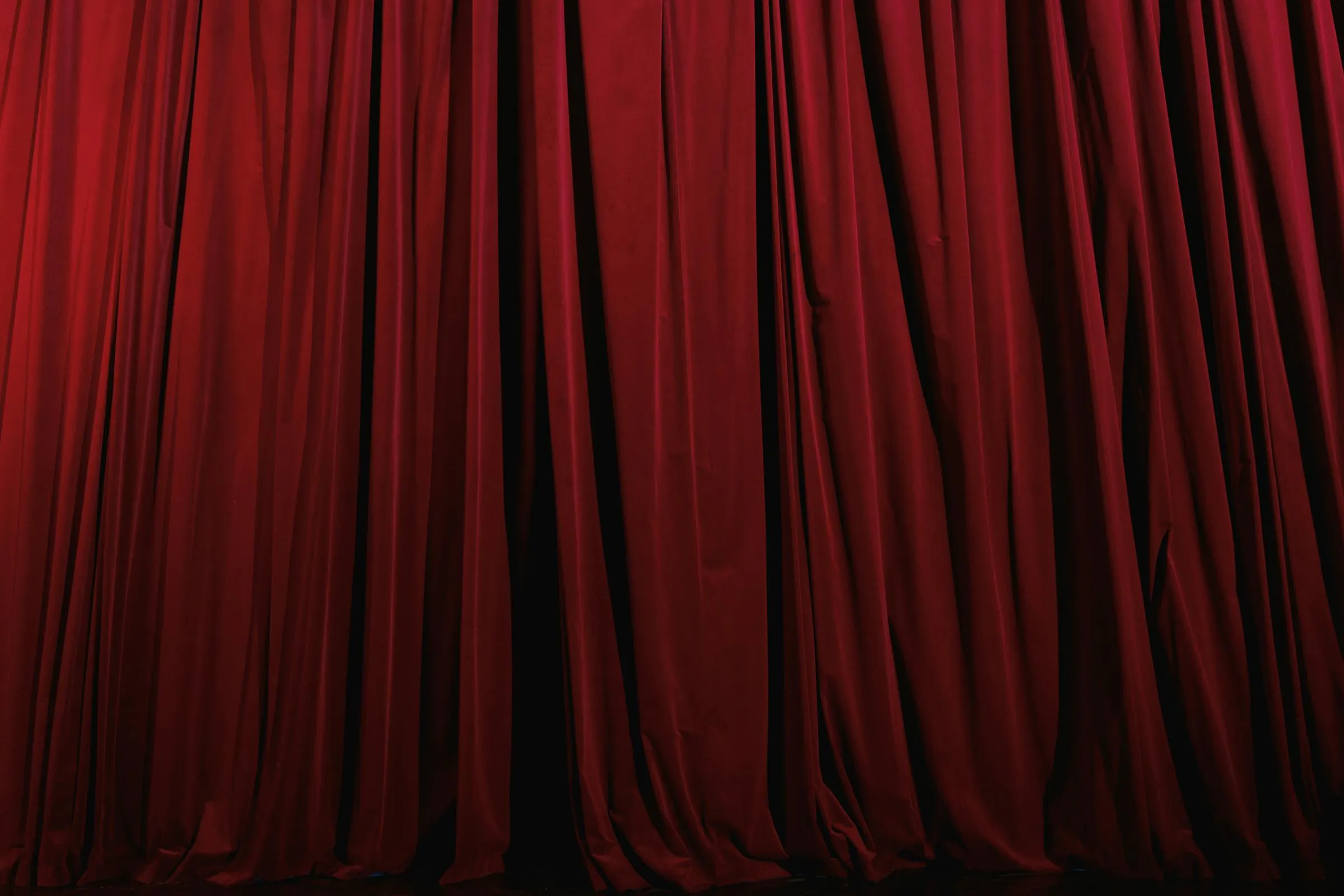 A heavy red theater stage curtain drawn closed under stage lighting
