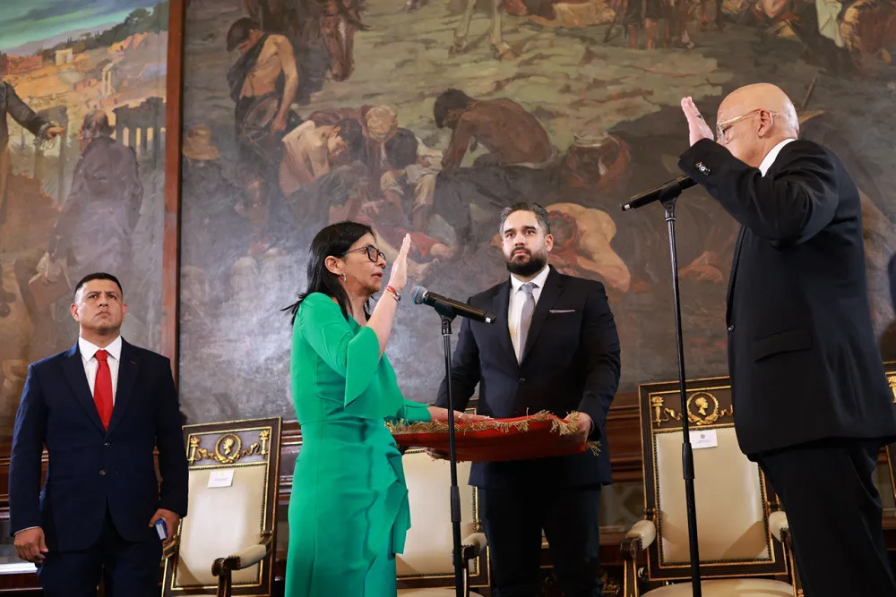 Delcy Rodríguez standing at a podium and taking the oath of office, surrounded by Venezuelan officials in a formal government chamber.
