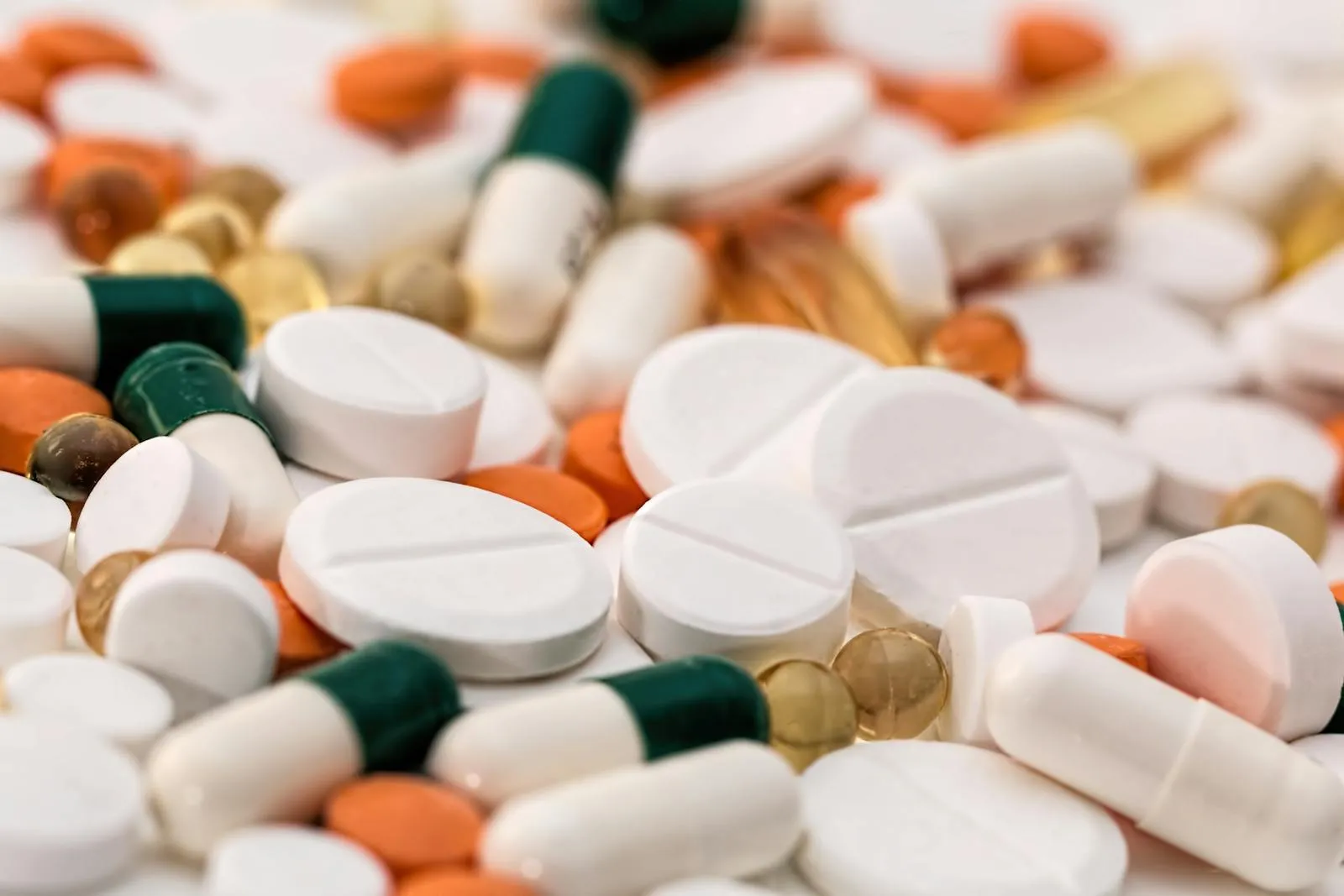A collection of white, orange, and green prescription pills and capsules spread across a white surface