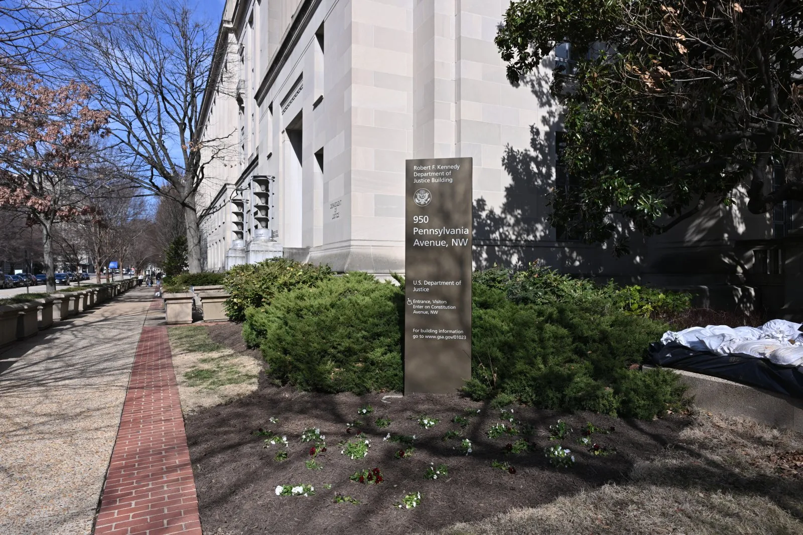 Corner of the Robert F. Kennedy Department of Justice Building in Washington, D.C., showing the stone facade and carved lettering of the DOJ sign against a clear sky