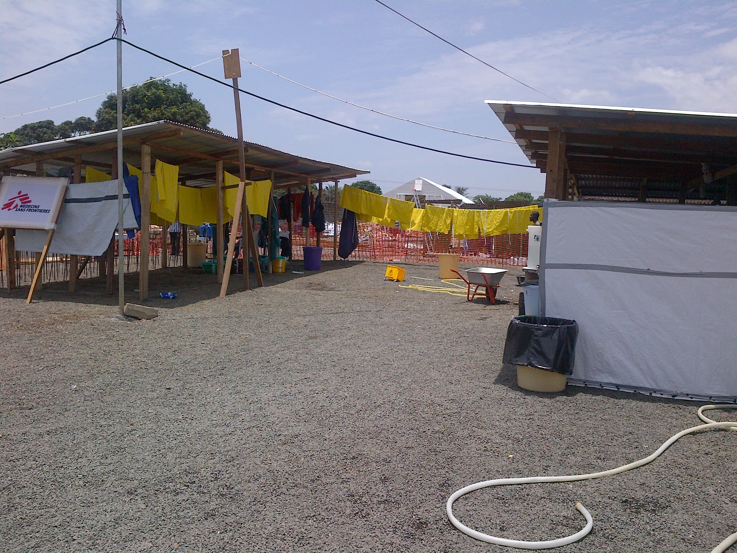 Health workers in full personal protective equipment—white hazmat suits, face shields, and gloves—at an open-air Ebola treatment unit, preparing to enter the isolation zone