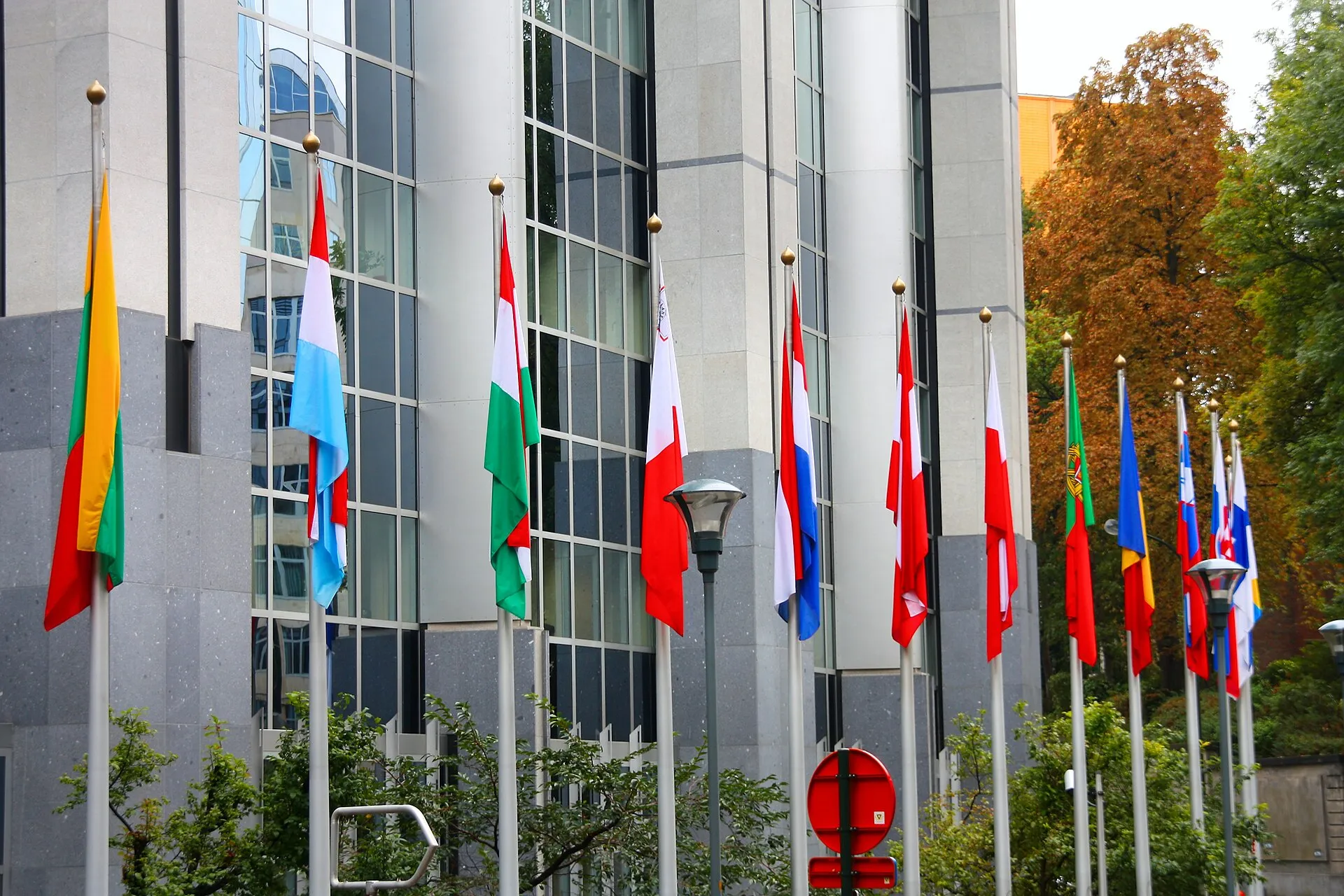 Rows of European Union member-state flags flying on poles in front of the European Parliament building in Brussels