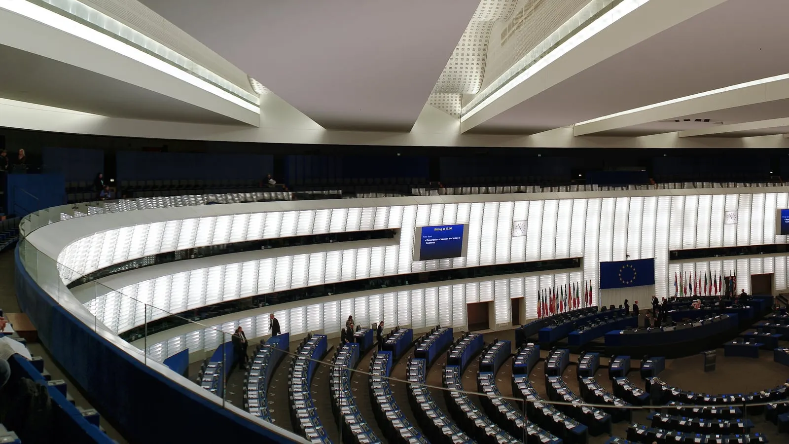 Interior view of the European Parliament's plenary chamber in Strasbourg, with rows of empty curved seating and the central podium in the foreground.