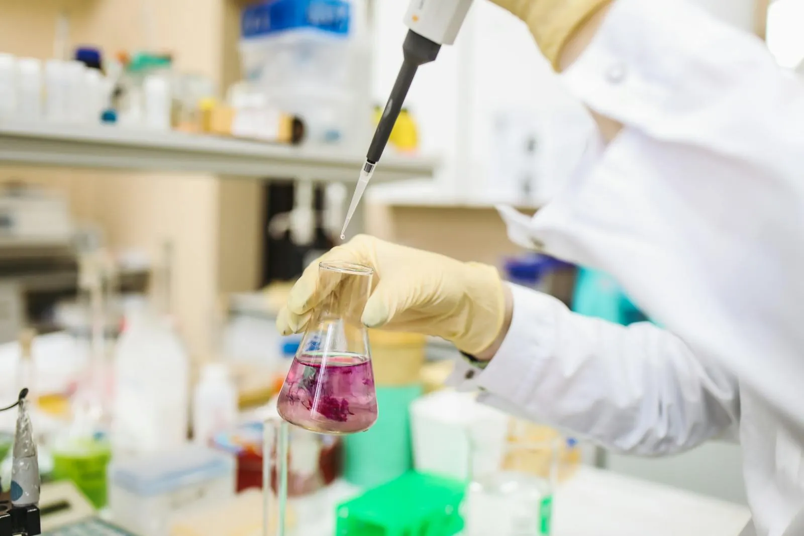 A scientist in a white lab coat examining samples at a laboratory workstation with specialized equipment in the background.