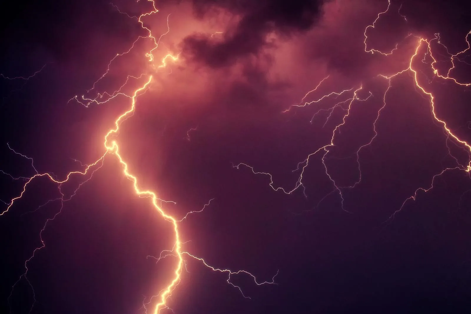 Bright lightning bolts branching across a dark purple and red storm sky at night