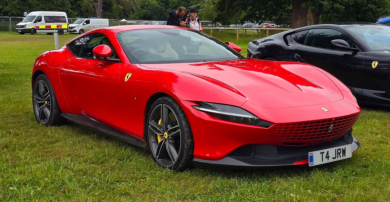A red 2021 Ferrari Roma grand tourer displayed at an auto show, viewed from the front-left angle