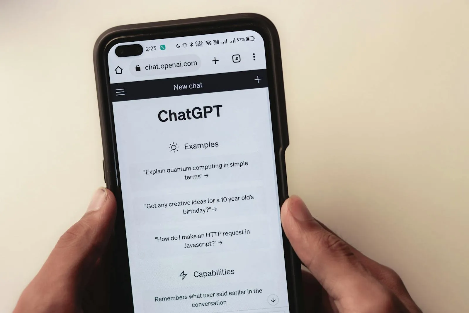 A smartphone held in one hand displaying the ChatGPT webpage on OpenAI's site, showing the chatbot's examples and limitations.