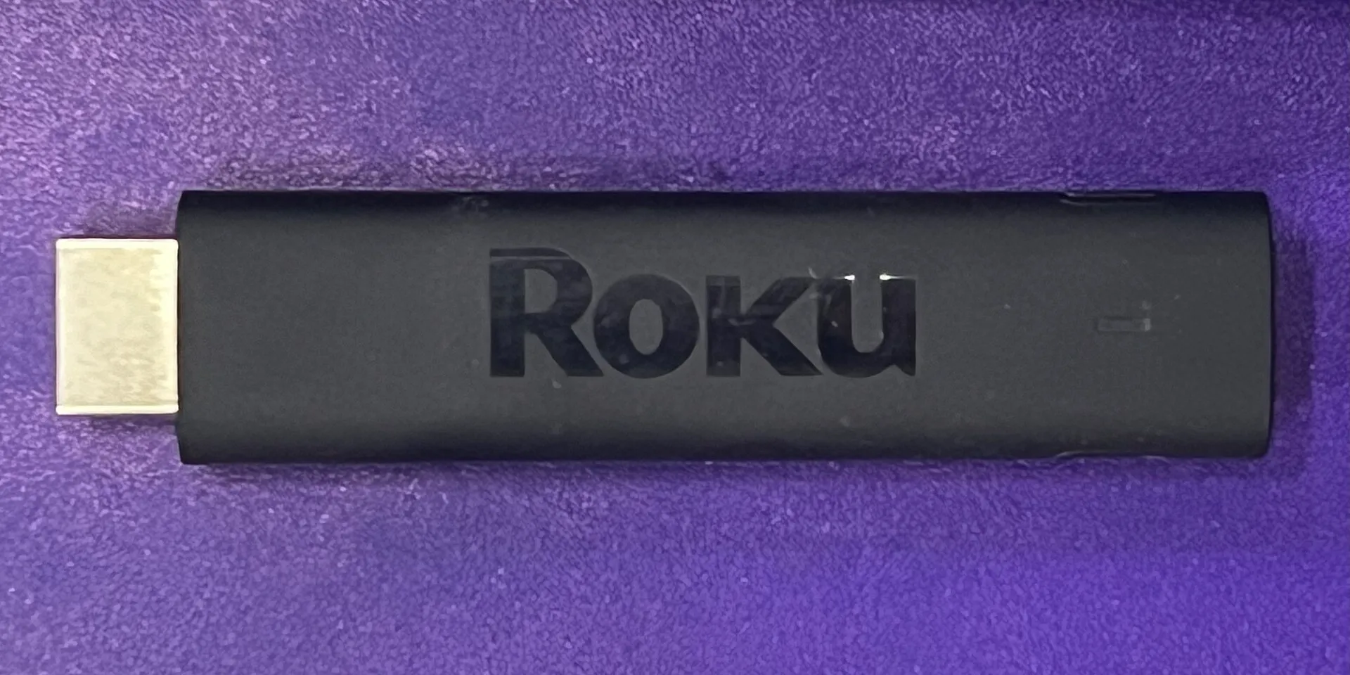 A Roku streaming stick and remote control resting on a surface in front of a television.