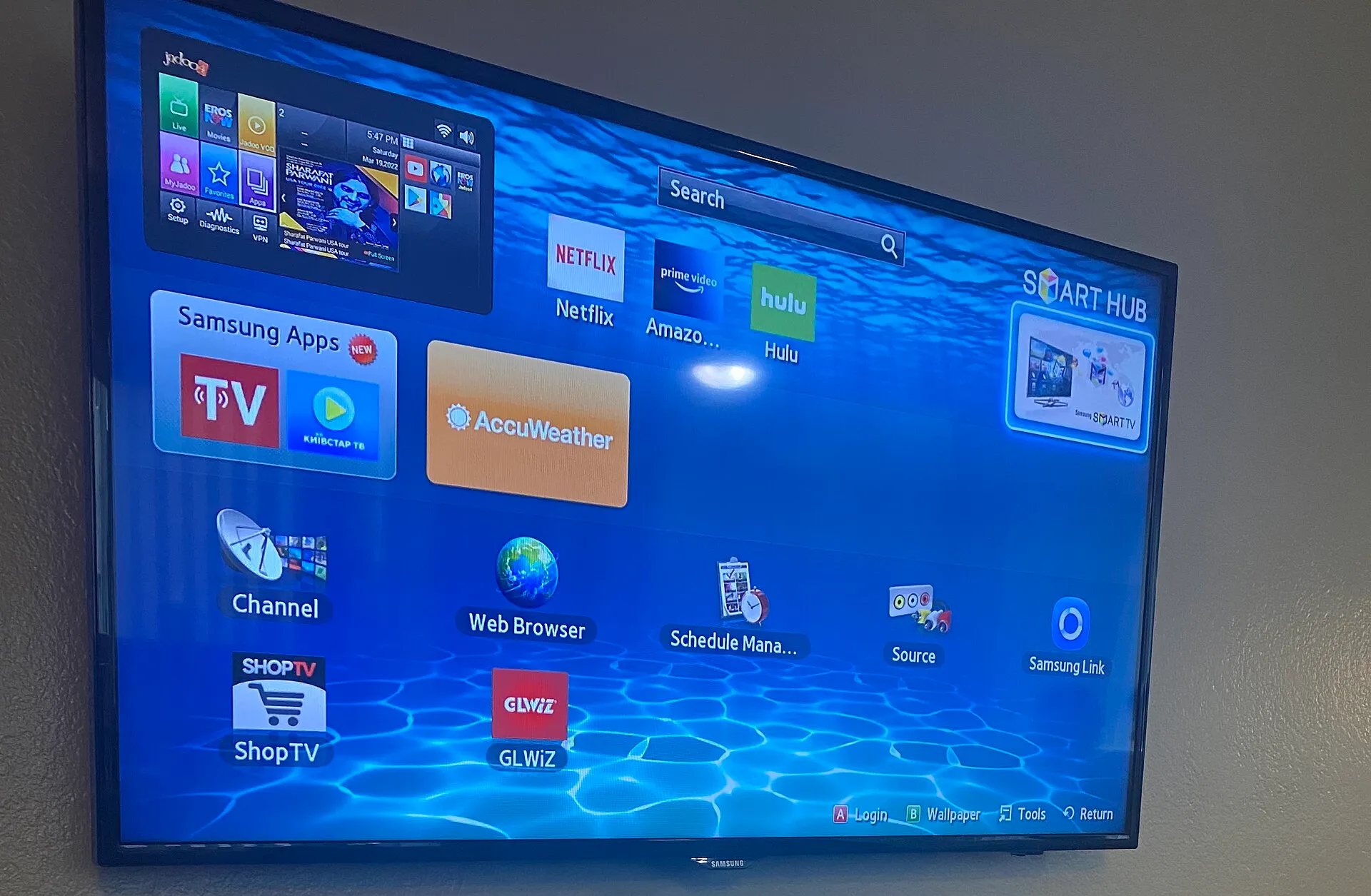 A wall-mounted smart TV displaying a home-screen menu of streaming app tiles including Netflix, Prime Video and Hulu.