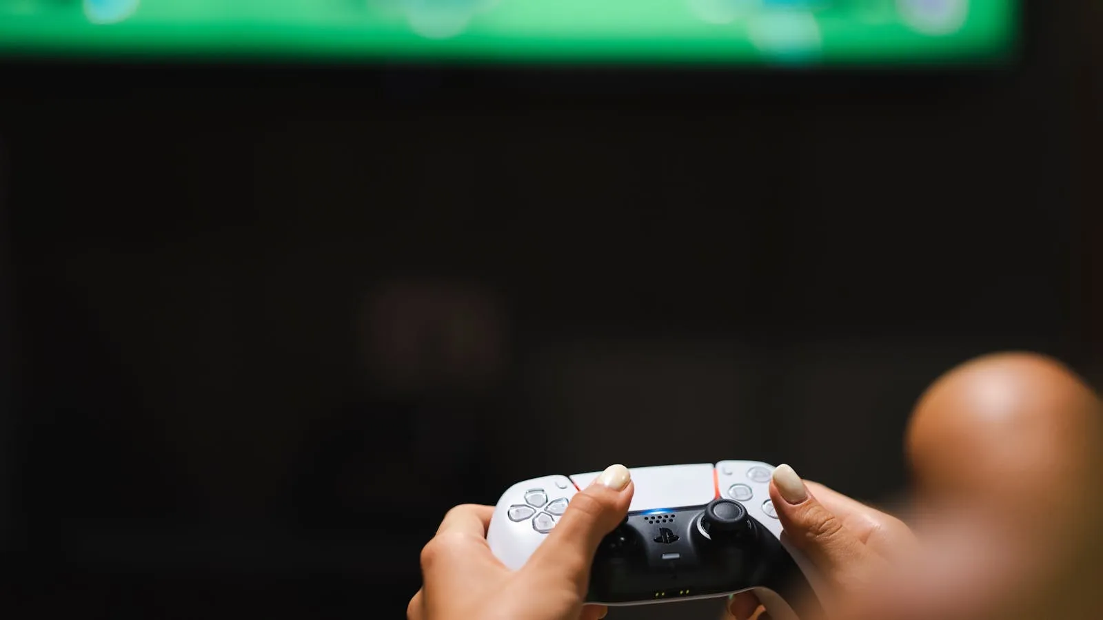 Two hands holding a white-and-black game controller in front of a softly blurred television screen