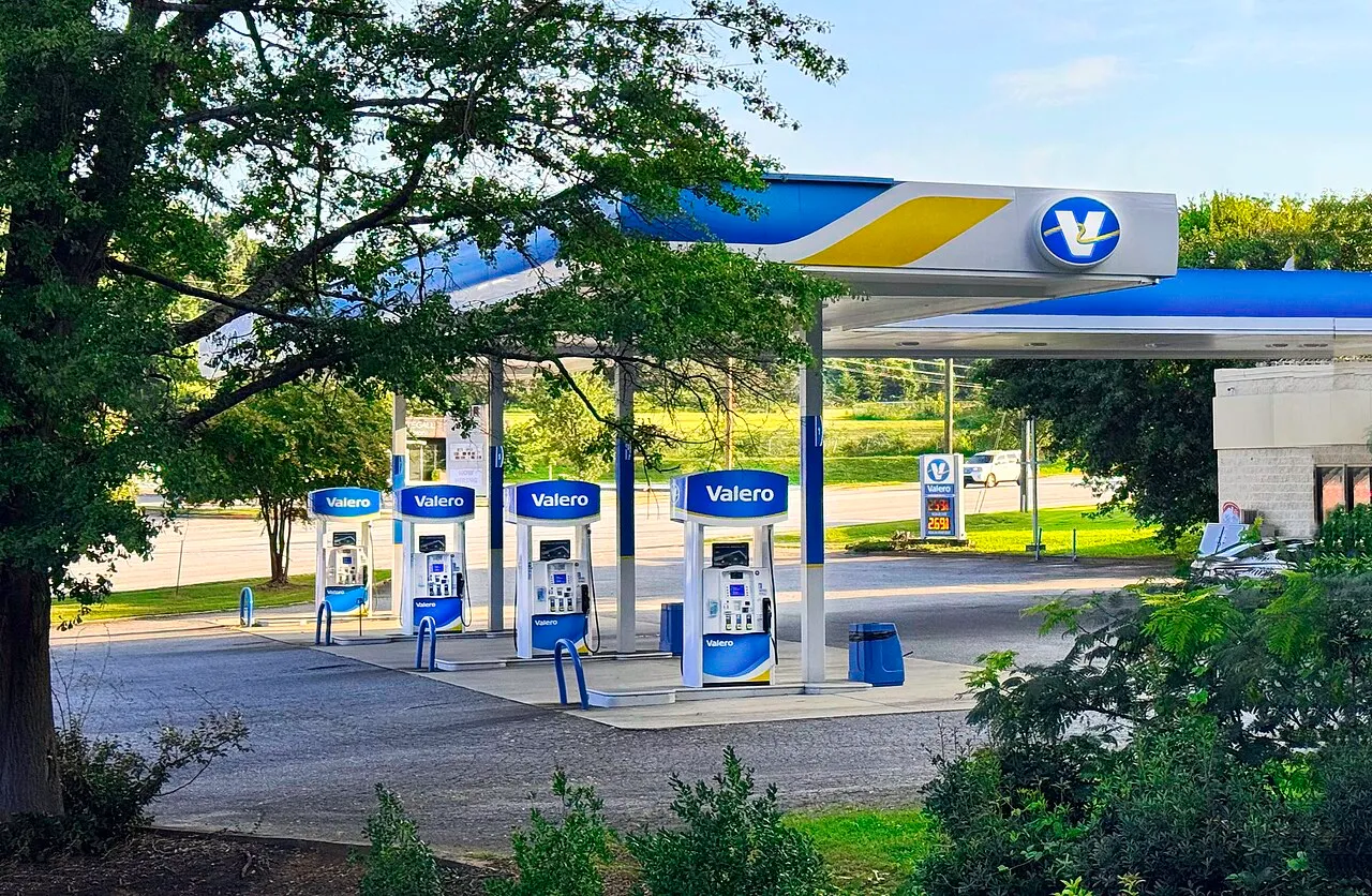Fuel pumps with hoses and nozzles at a Valero gas station beneath a canopy on a clear day.