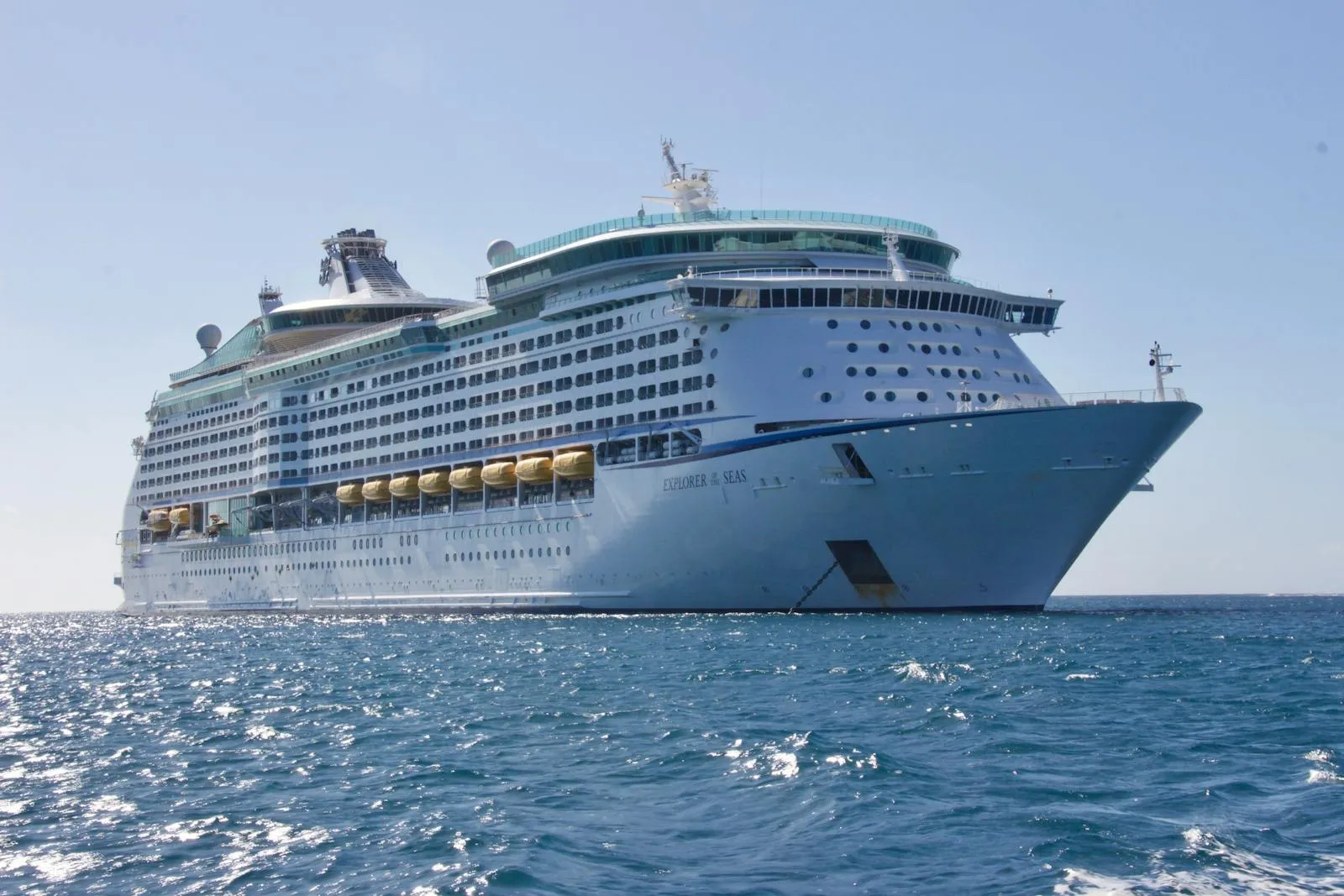 A large white cruise ship sailing through calm blue open water, photographed from a low angle showing the full broadside profile of the vessel