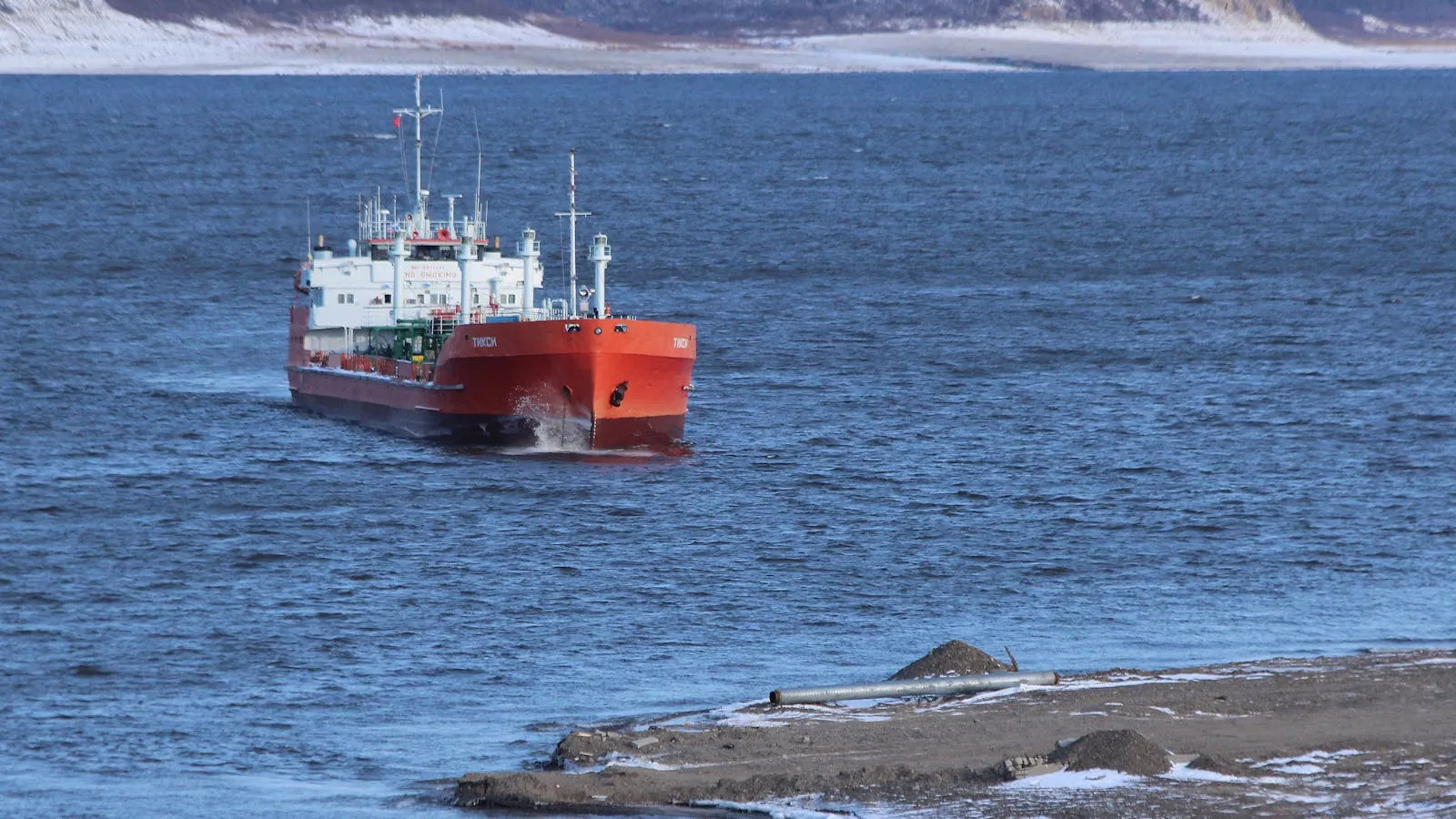 A large oil tanker ship at sea with a gray sky and calm ocean water in the background