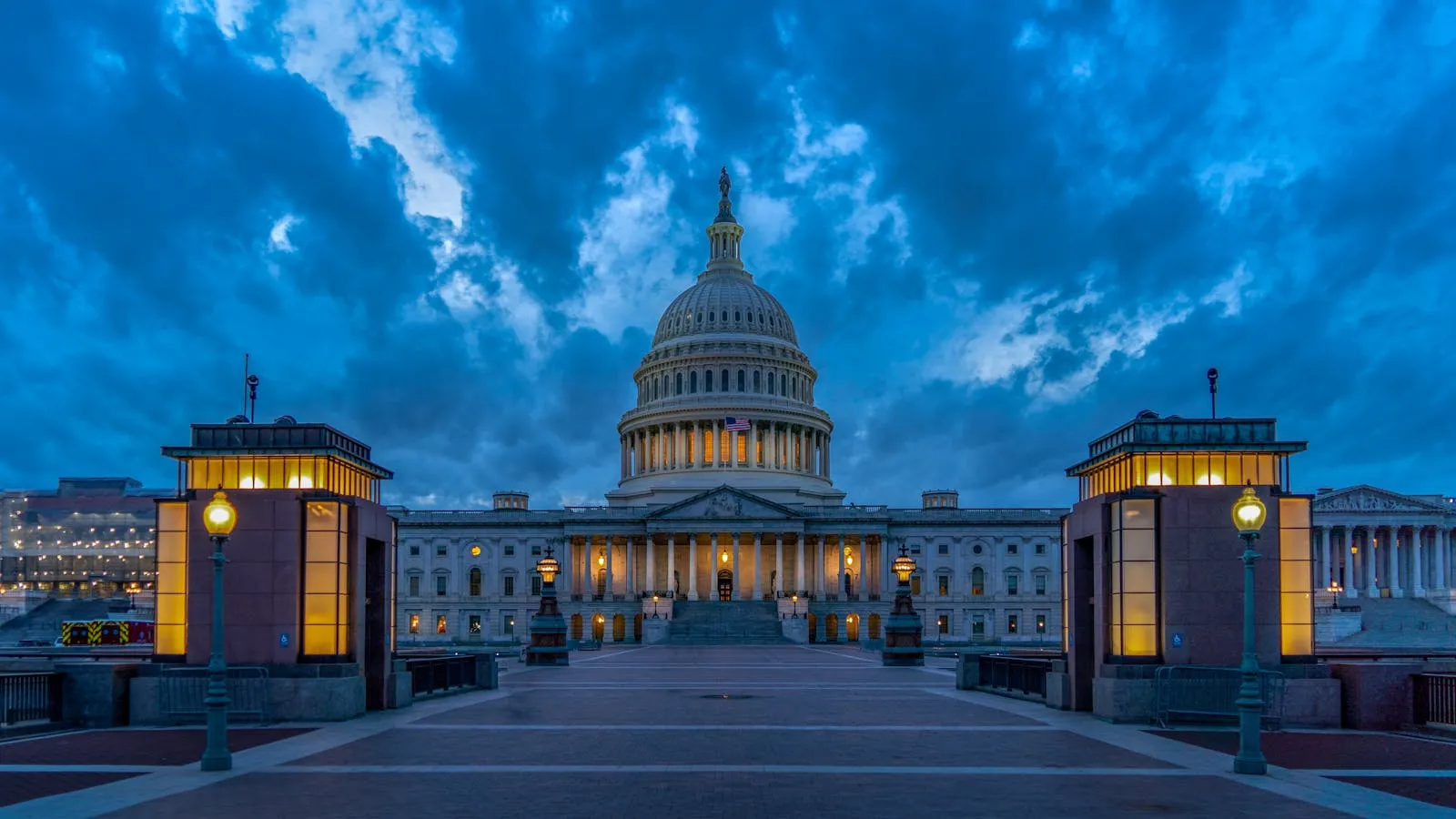 The United States Capitol dome lit against a dark night sky, reflected light on the surrounding grounds
