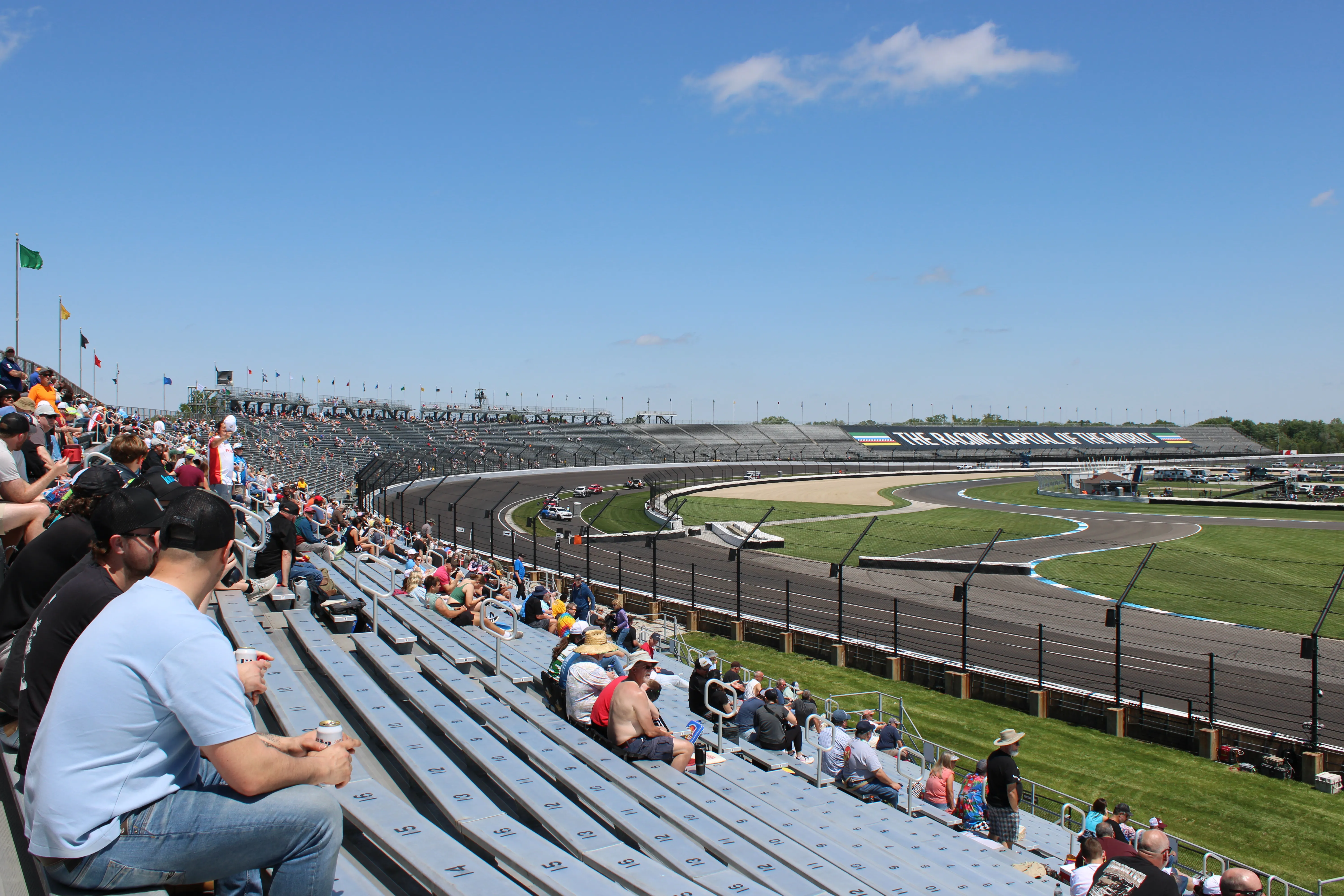 Indianapolis Motor Speedway main grandstand and front straight on a clear May day, empty bleachers, pit lane visible.