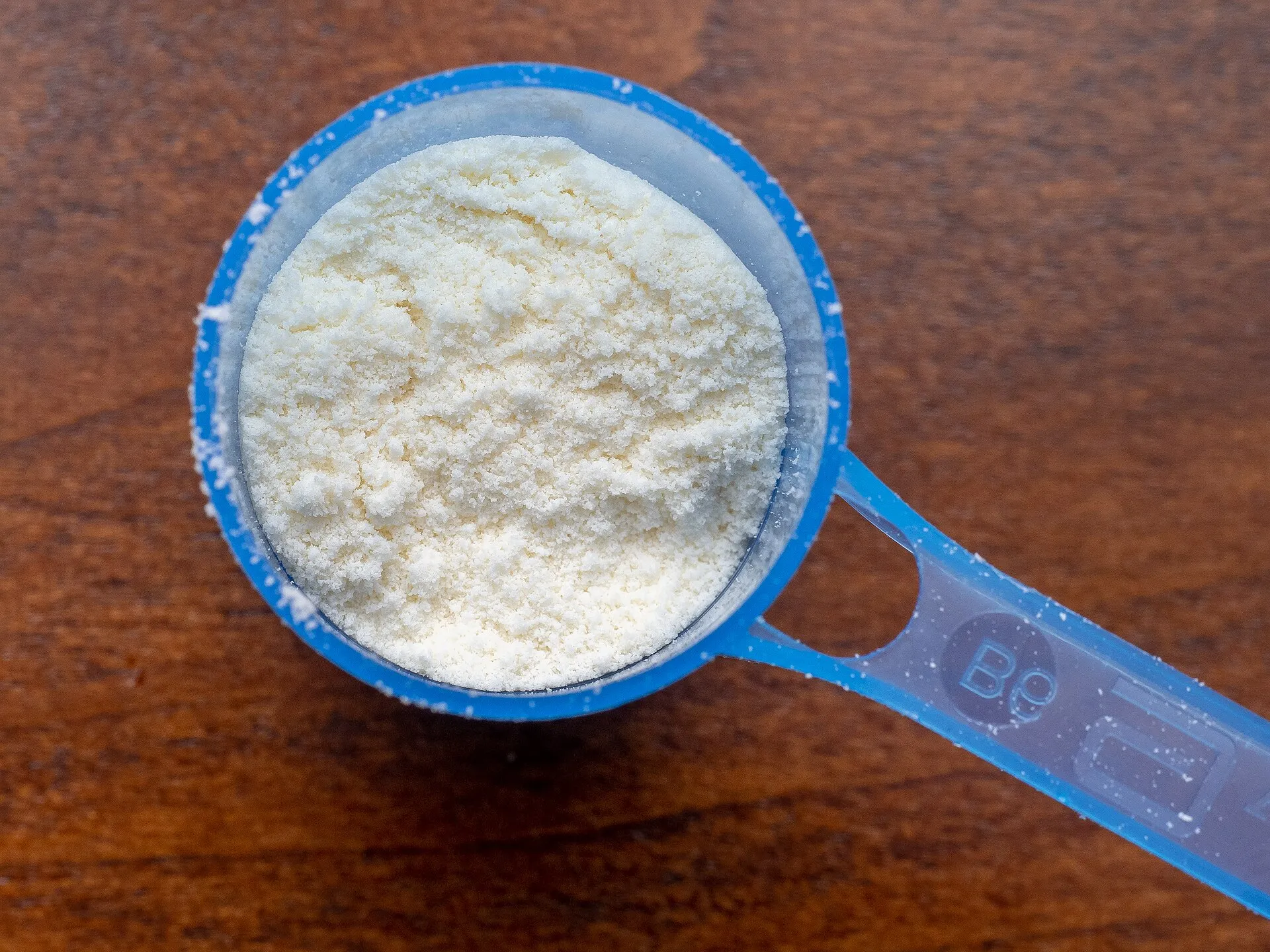 A blue plastic scoop filled with white powdered infant formula resting on a wooden surface.