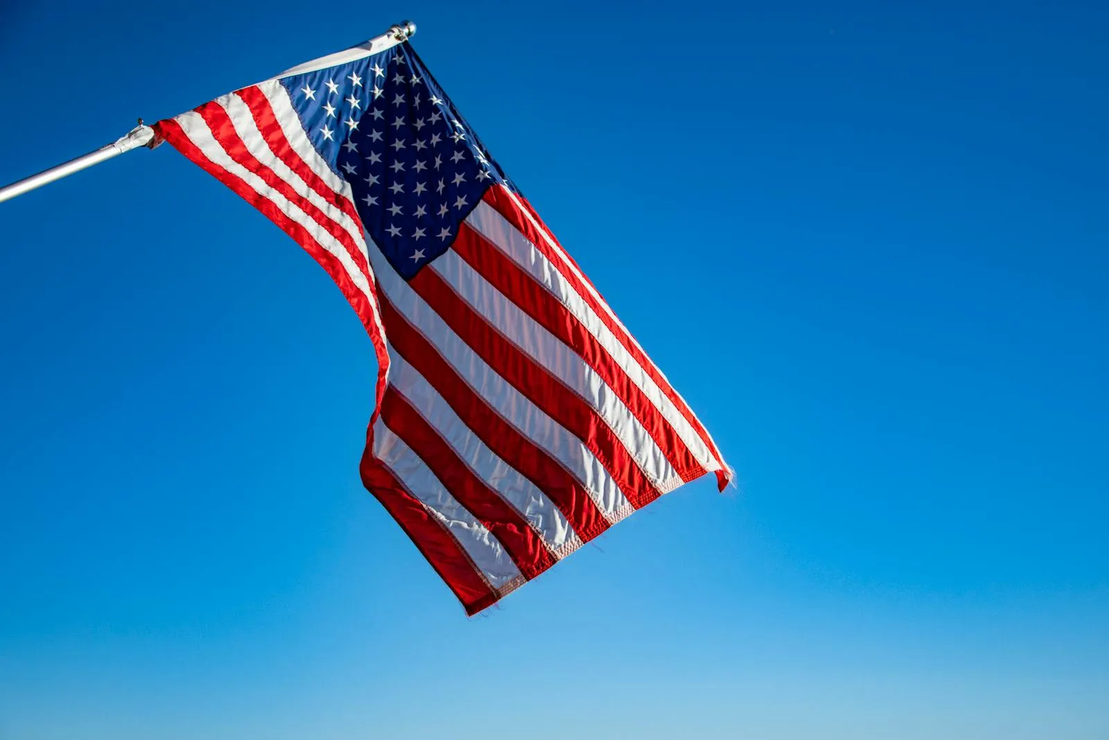The American flag flies on a white pole against a clear blue sky.