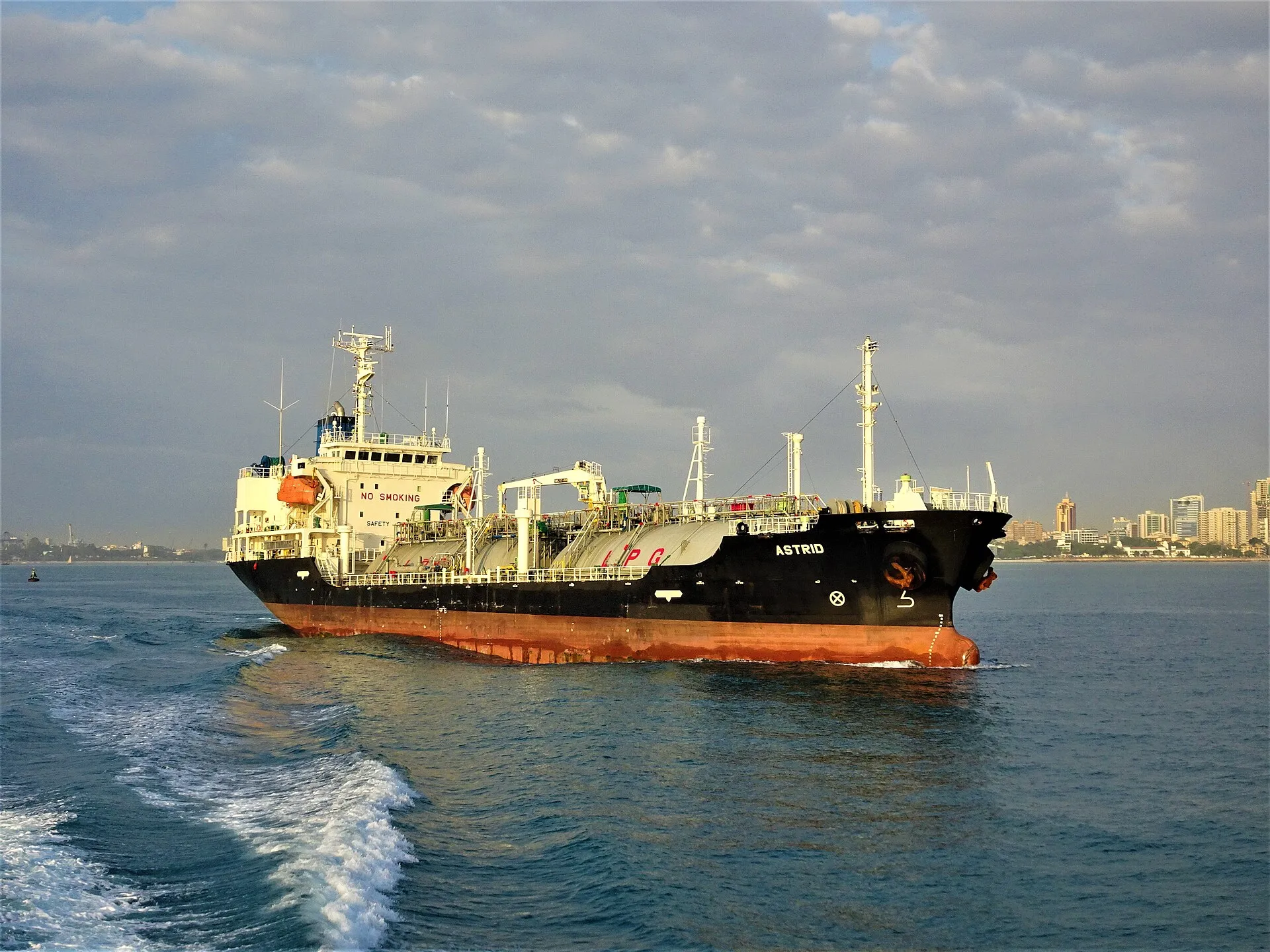 A laden petroleum tanker under way on open water, photographed from astern as it leaves port.