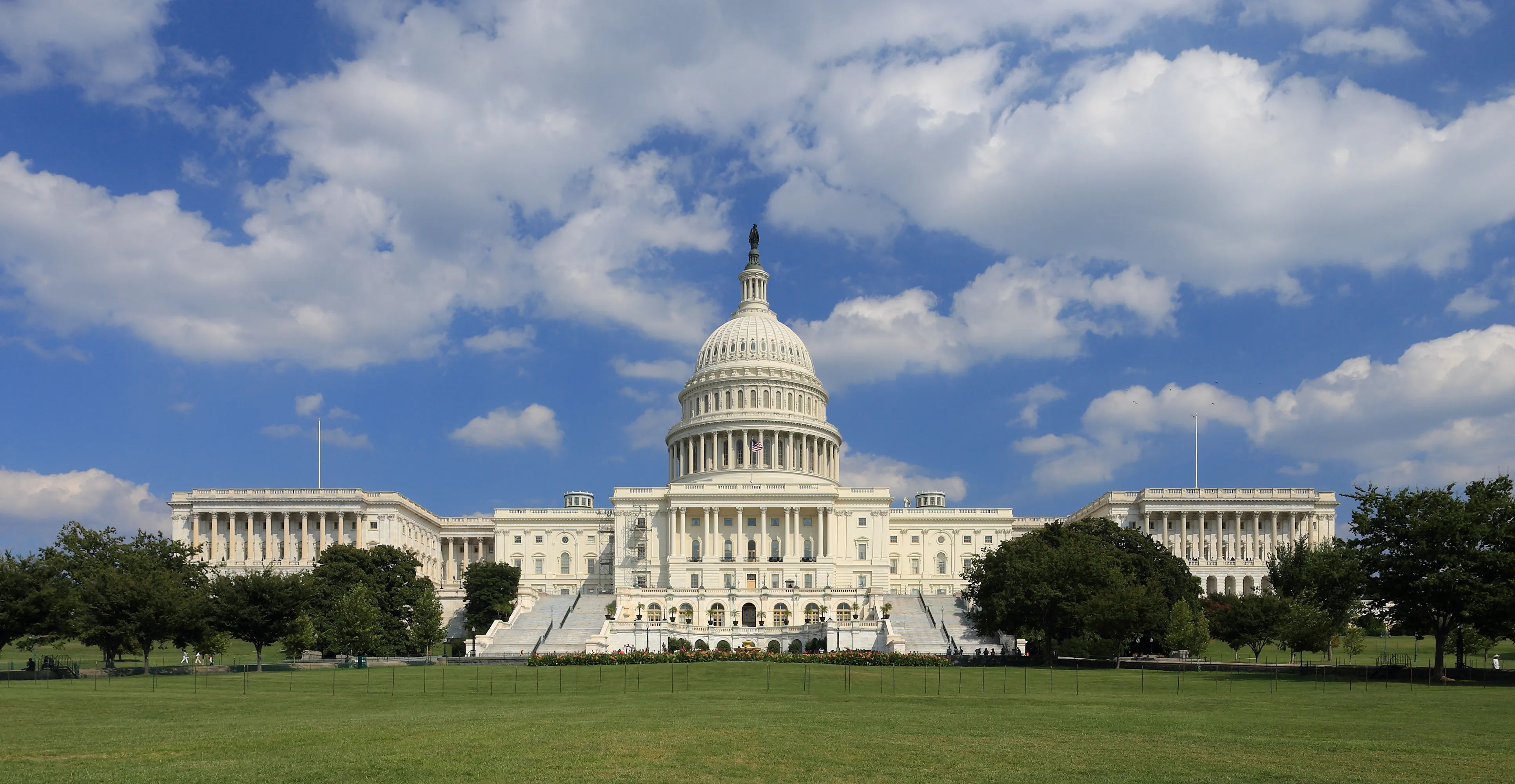 The western front of the United States Capitol building with both the Senate and House wings flanking the central dome, photographed against a partly cloudy sky