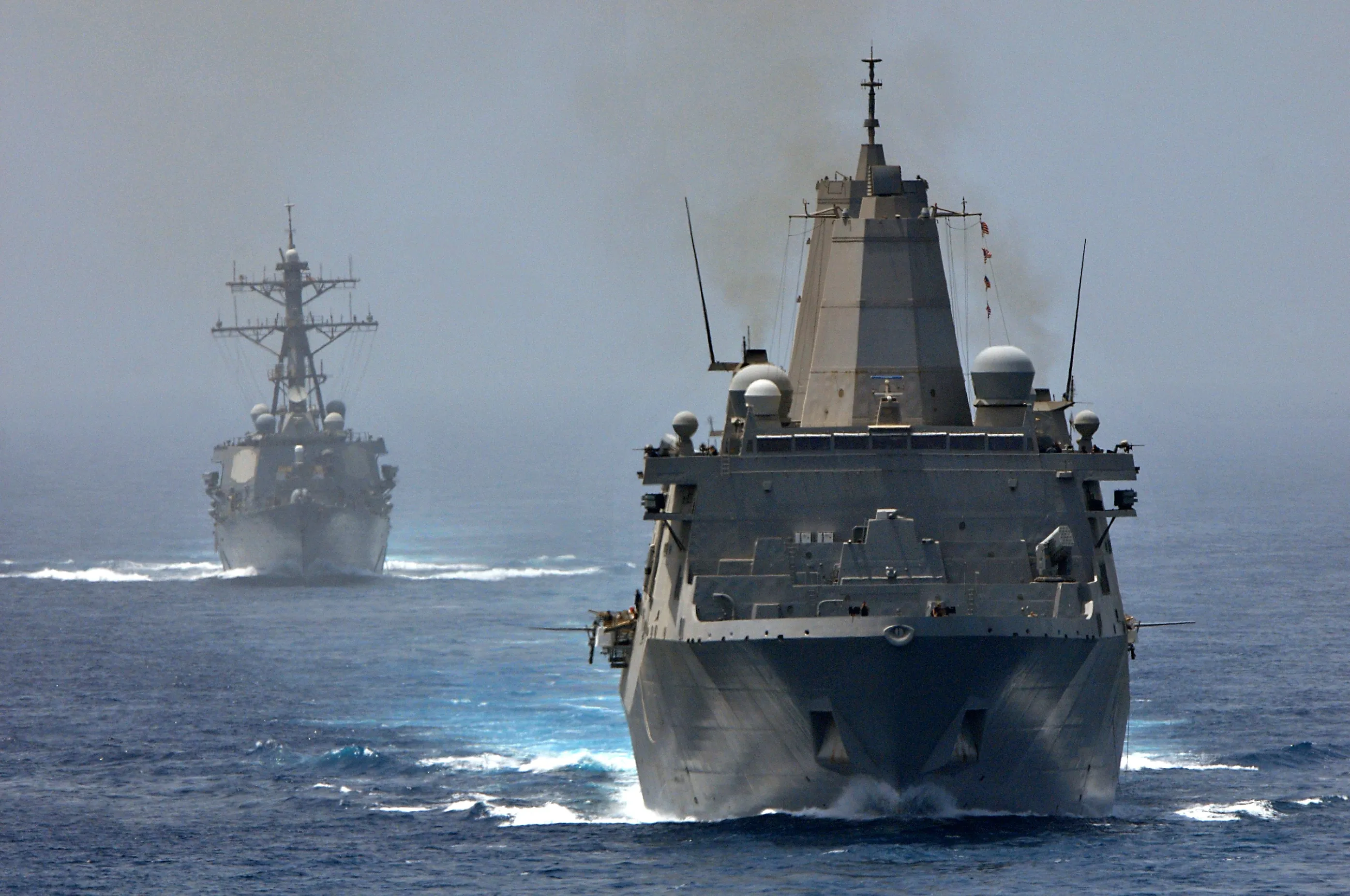 Two gray U.S. Navy warships steaming in formation on open sea under a hazy sky.