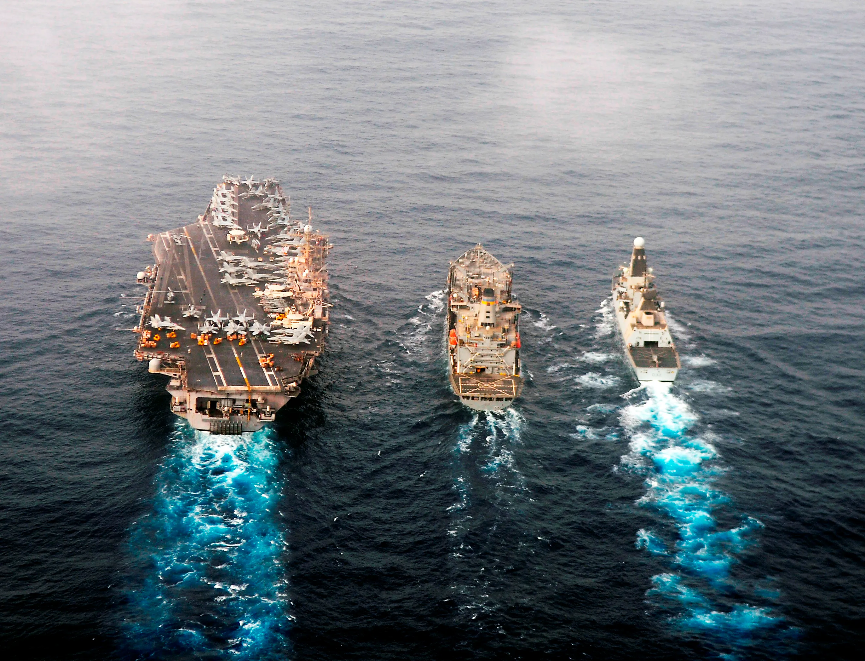 The USS Abraham Lincoln aircraft carrier and two other naval vessels conducting a replenishment-at-sea operation on open water, photographed from an aerial perspective.