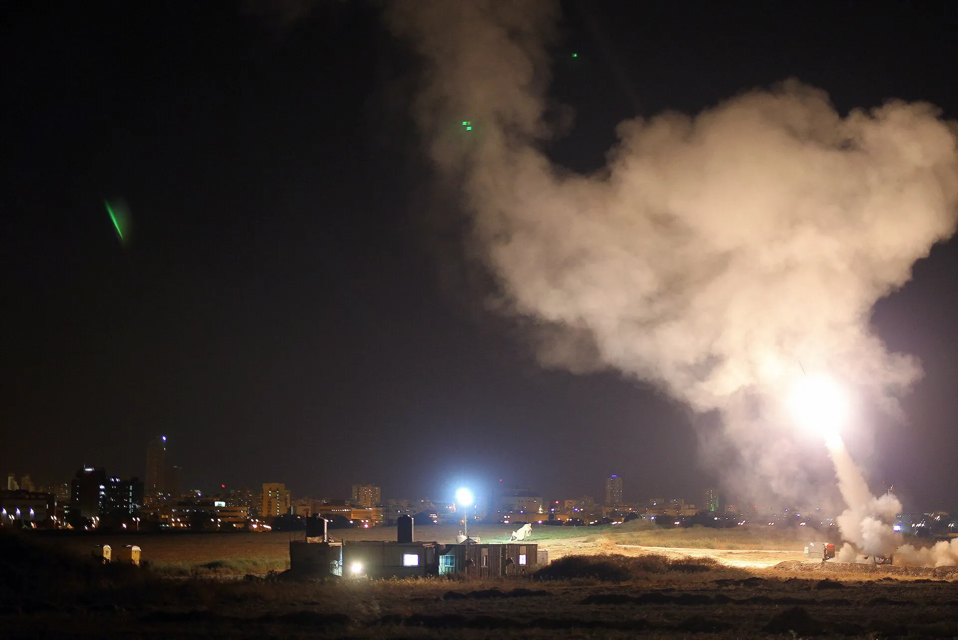 Streaks of light from Iron Dome interceptor missiles rising into a dark sky over an Israeli town.