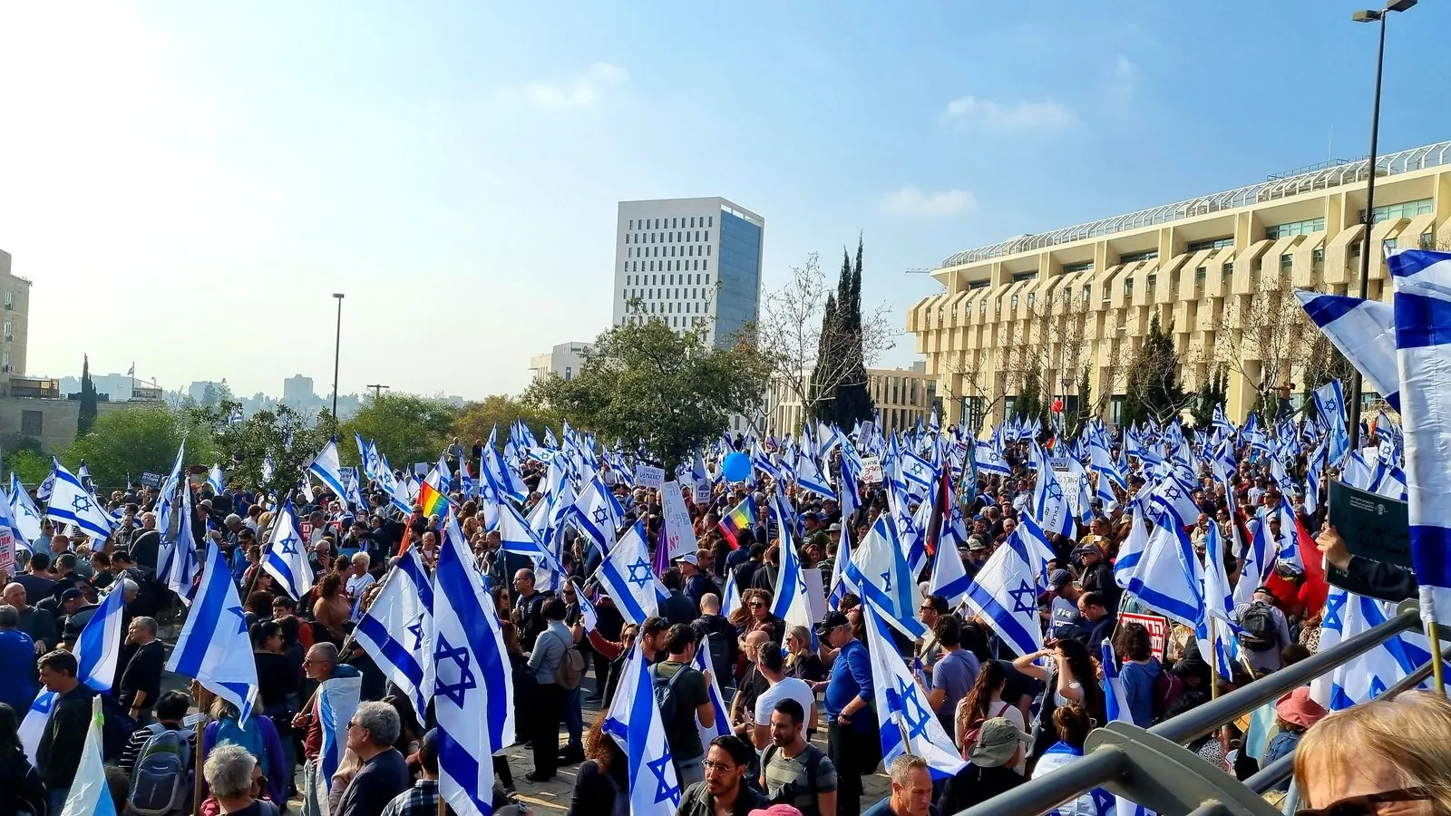 A dense crowd of demonstrators fills a Jerusalem plaza, waving hundreds of blue-and-white Israeli flags.