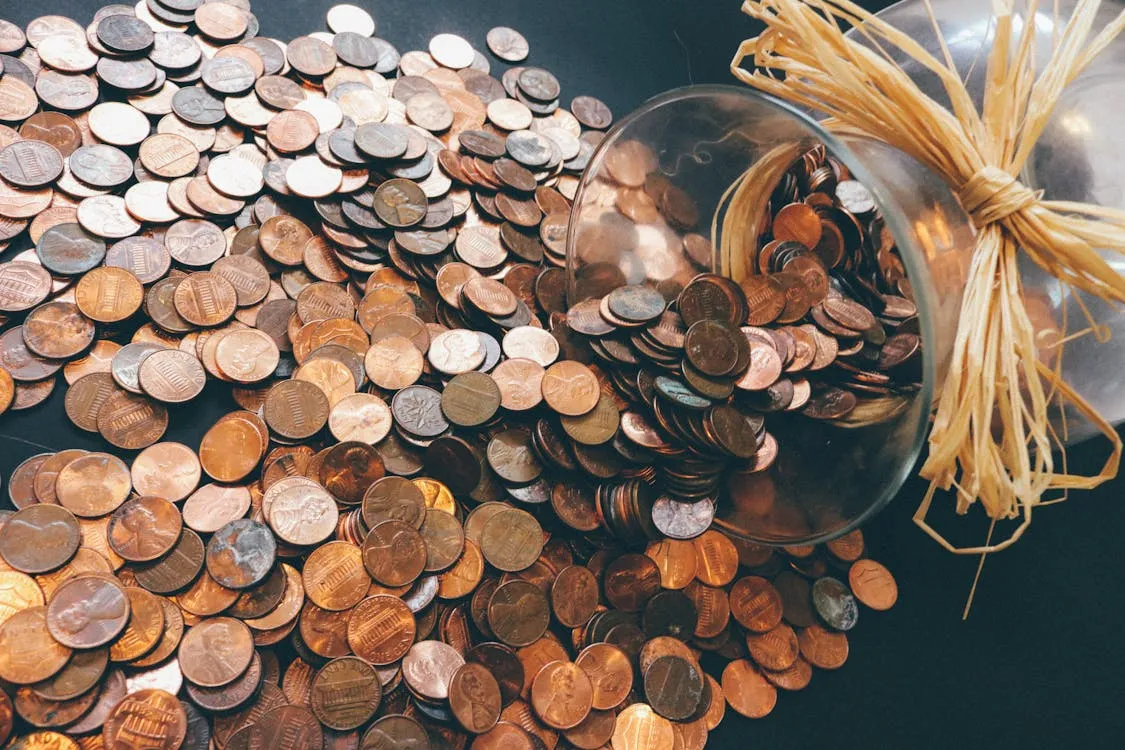 A glass jar tipped over with US pennies spilling out across a dark surface.
