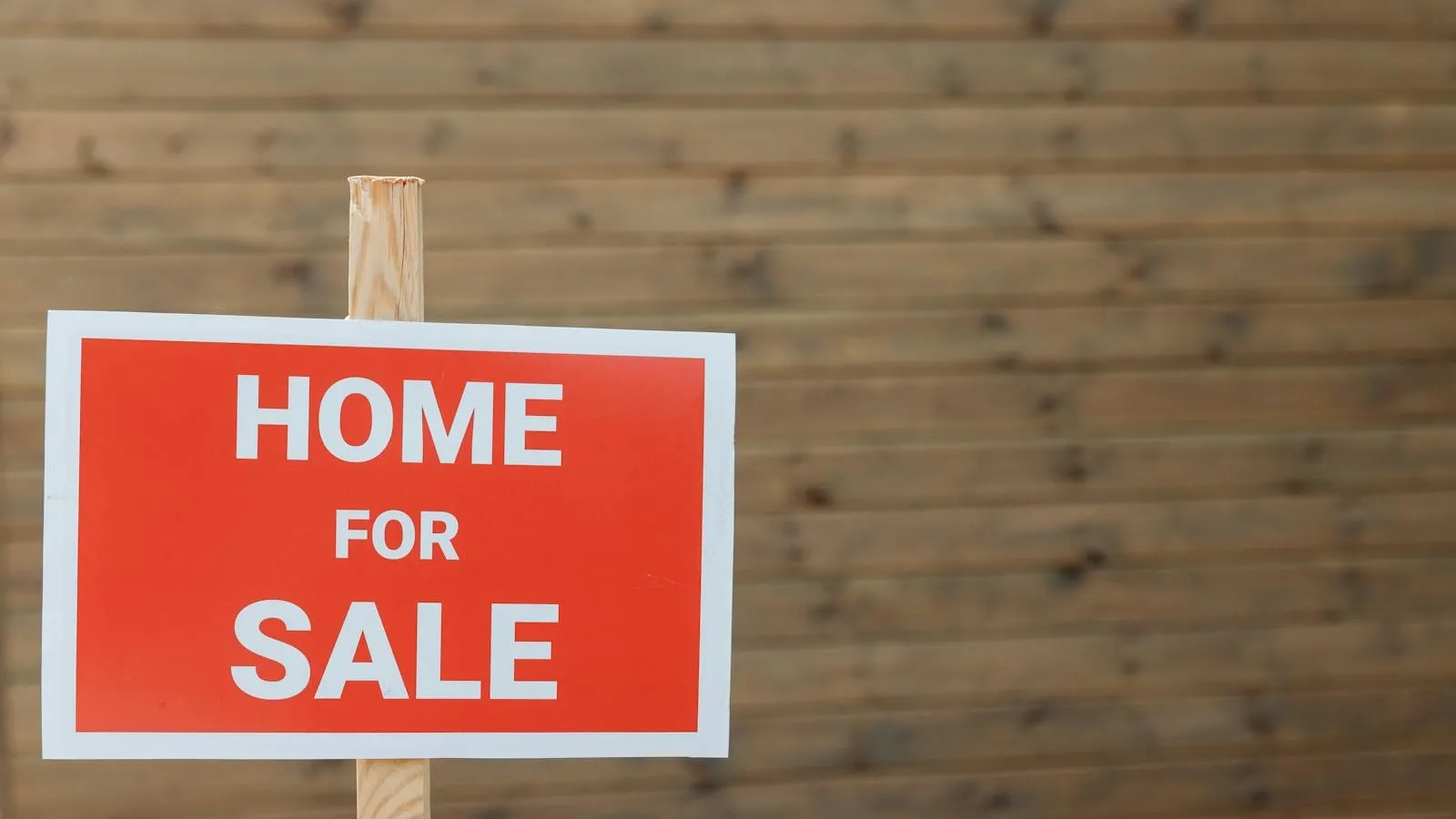 A 'For Sale' sign in front of a suburban American house.