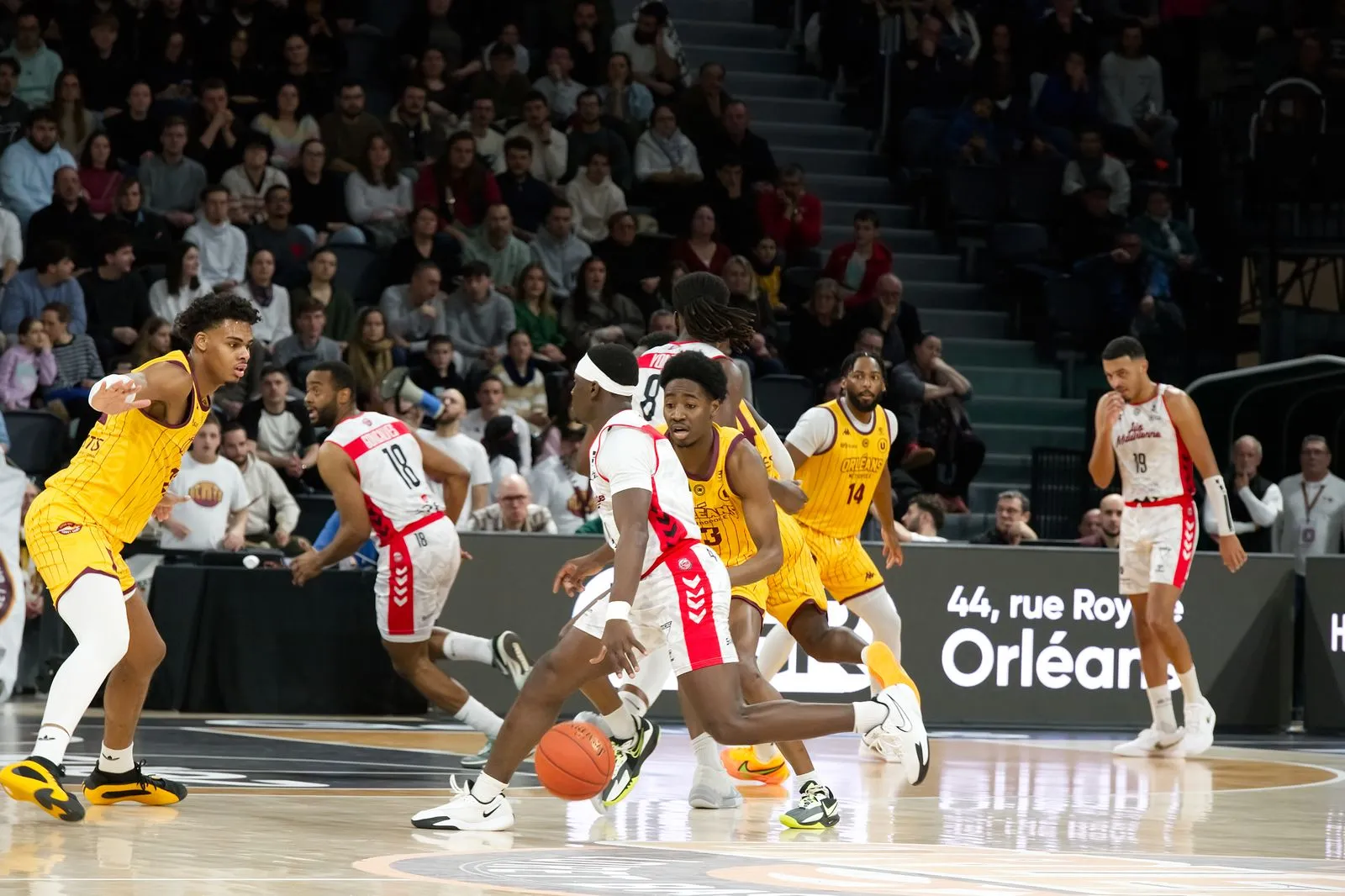 Players drive toward the basket during a professional basketball game in front of a packed arena crowd.