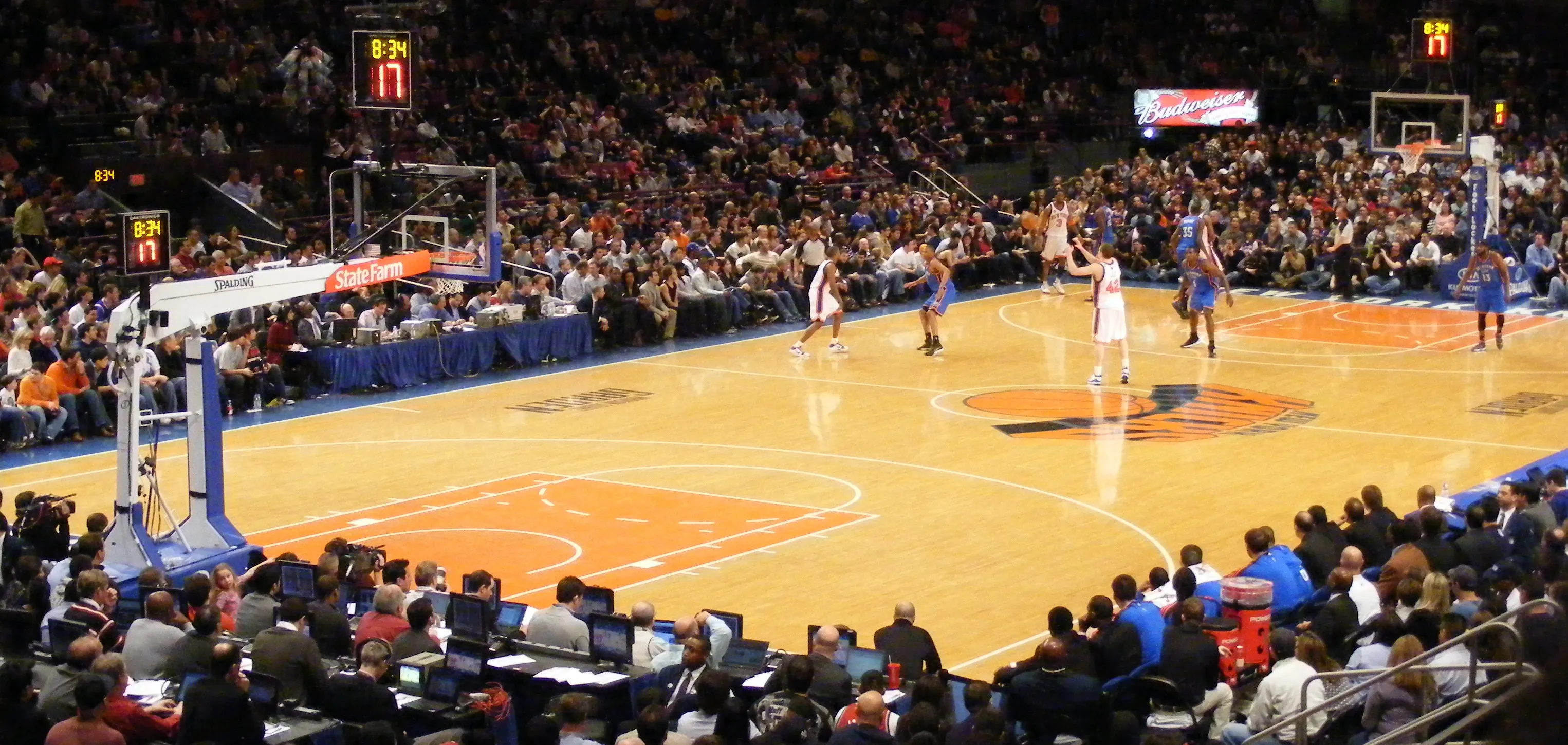 Wide-angle interior view of Madison Square Garden during an NBA game, showing the lit basketball court and fans filling the arena bowl from upper level