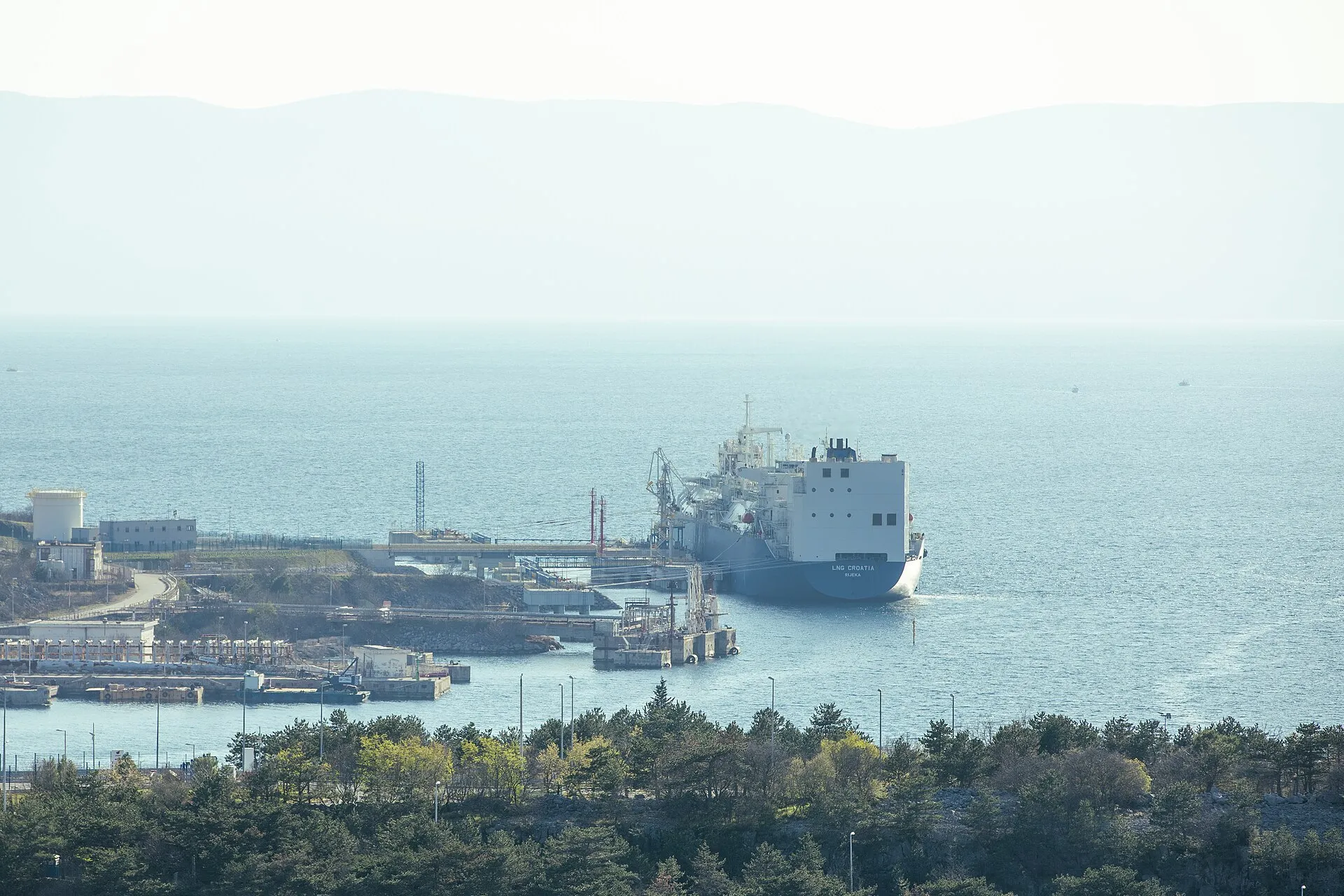 A large red and white oil tanker underway on the open sea on a clear day, viewed from above the bow.