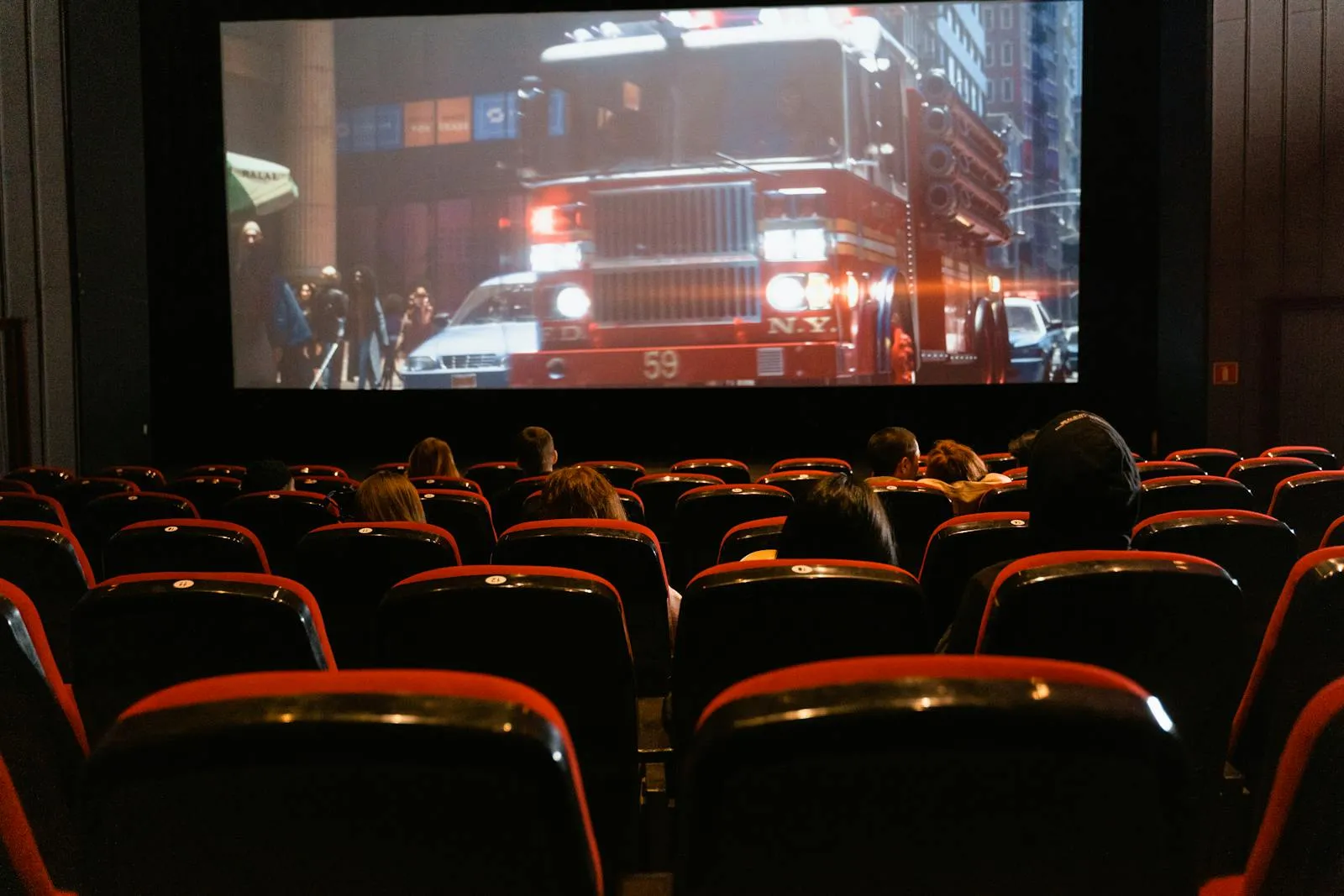 Silhouetted audience members seated in a darkened movie theater watching a film projected on the screen ahead of them