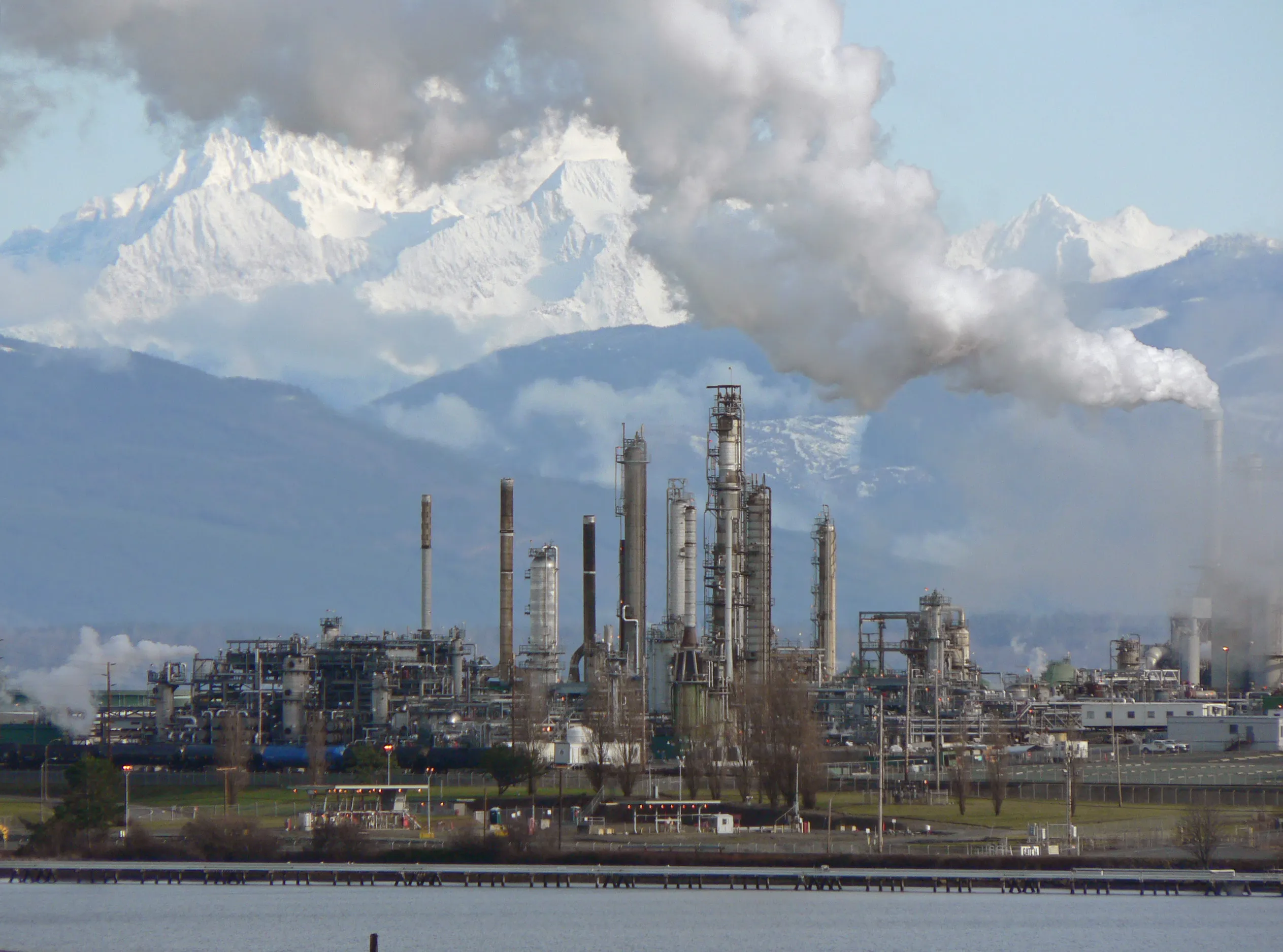 An oil refinery with towers, tanks and flare stacks viewed across water at dusk.