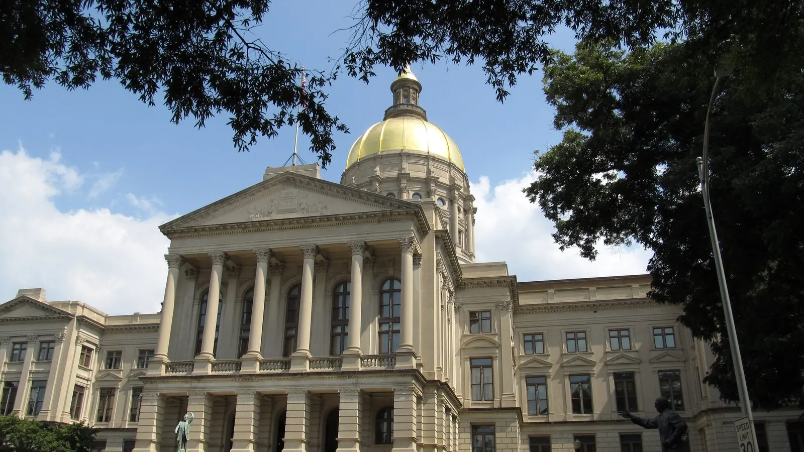 The gold-domed Georgia State Capitol building in Atlanta, seen from across its lawn under a blue sky.