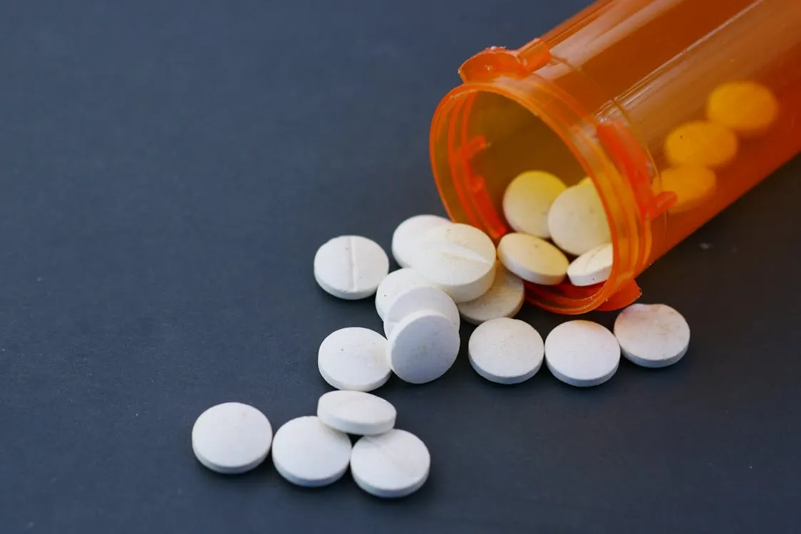 An orange prescription pill bottle tipped on its side with white round pills scattered across a dark surface