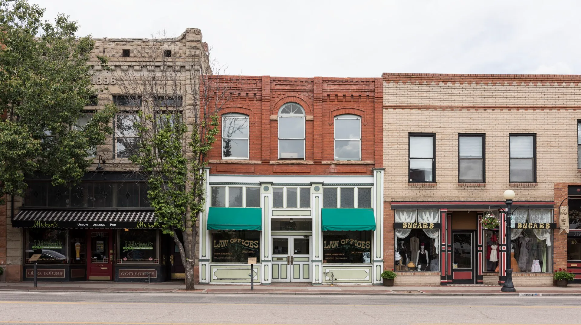 A row of brick storefronts with shop signs and awnings along a historic downtown commercial street.