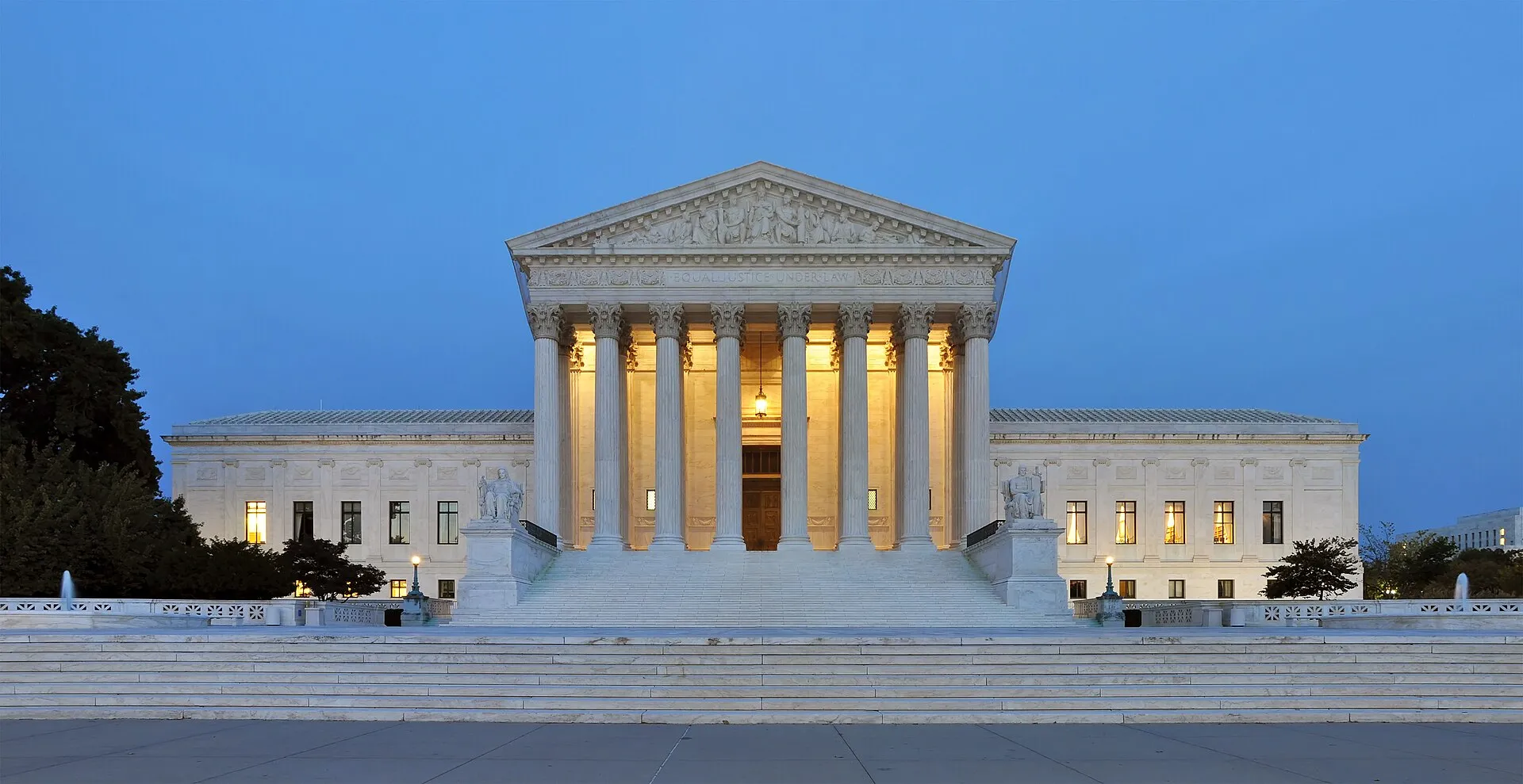 The west front of the U.S. Supreme Court building in Washington at dusk, its marble columns lit from within against a deep blue sky.